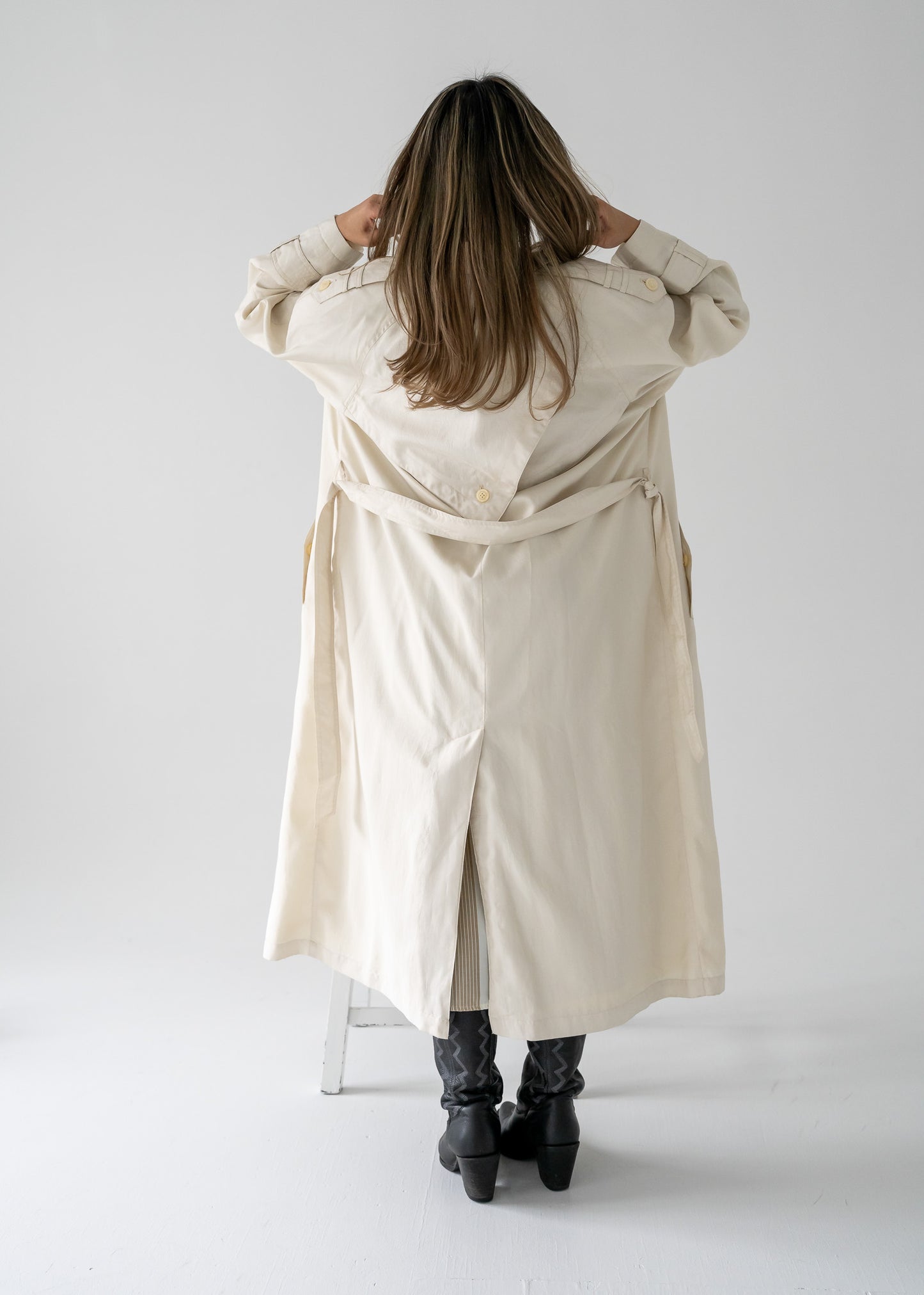Person wearing a vintage cream-colored, double-breasted, belted, full-length trench coat on a white background