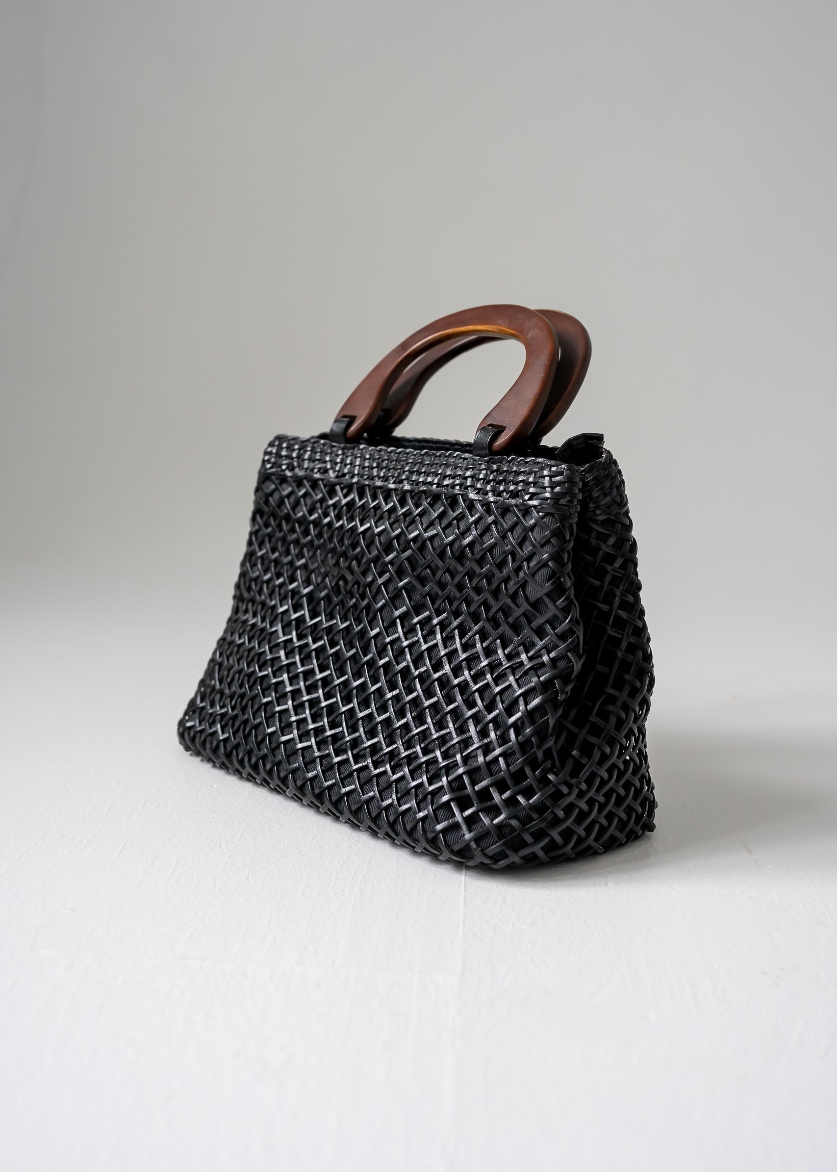 A vintage black leather handbag with an open basket weave pattern and wooden handles.