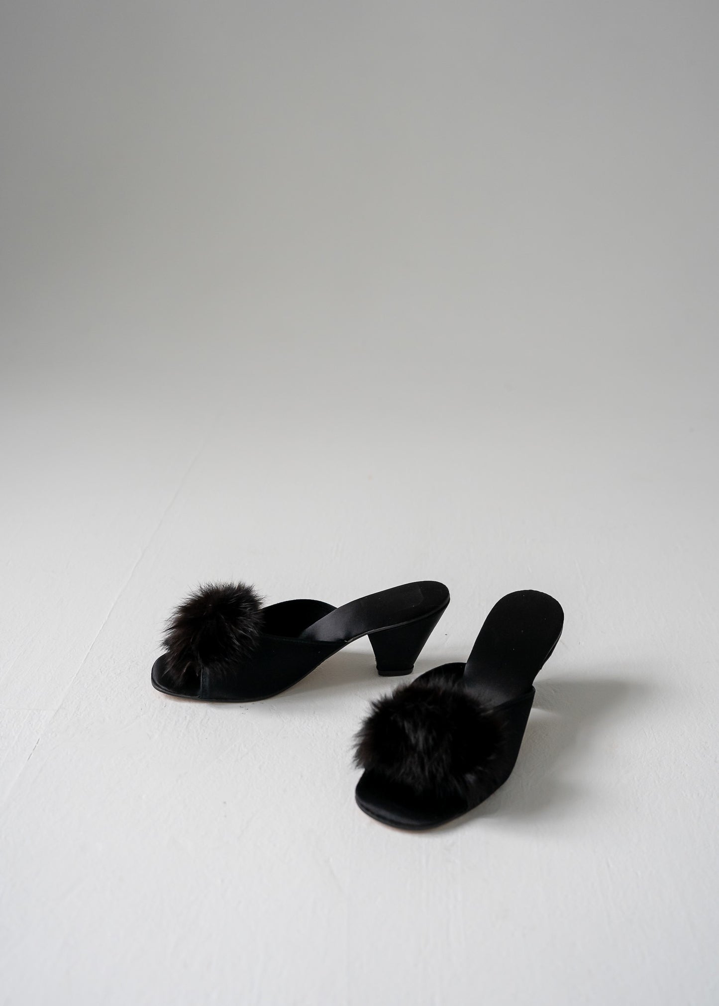 Black vintage kitten heels with fur pom-poms on a white background
