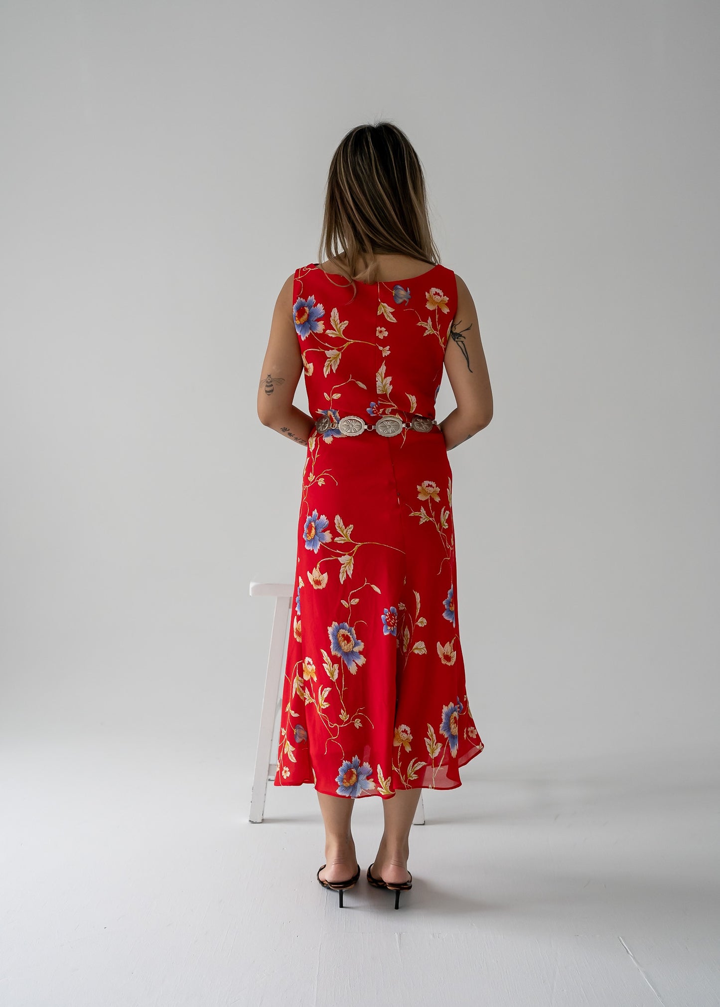 A woman wearing a bright red cowl neck bias cut floral summer dress back view