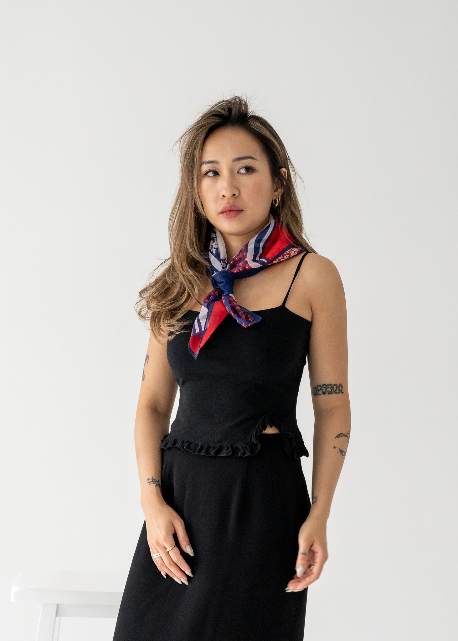 A woman wearing a vintage black tank top with a ruffle hem and a multicolored scarf around her neck.