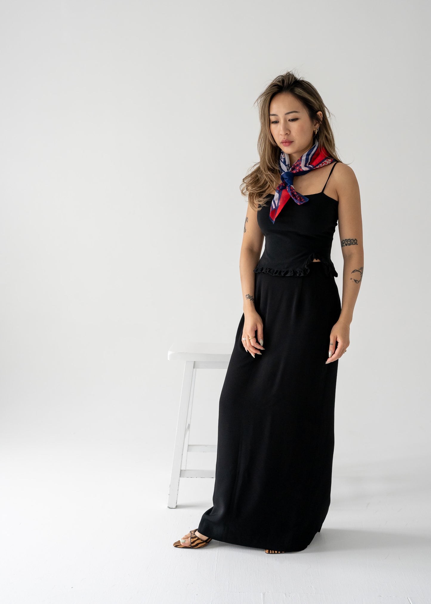 Woman in a vintage black column skirt and black tank top with a scarf standing against a white background