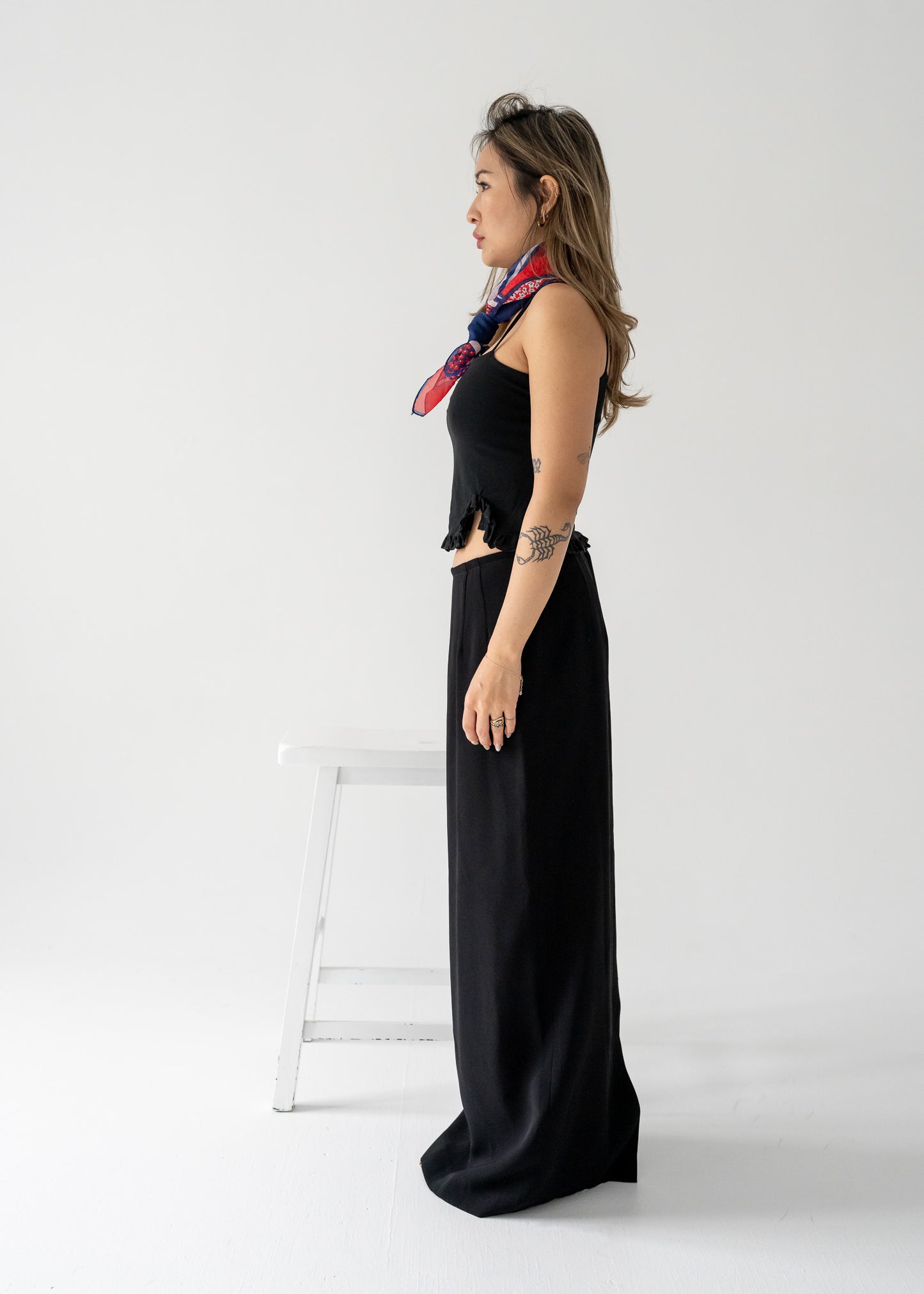 Woman in vintage black tank top with a ruffle hem and black column skirt with colorful scarf on a white background