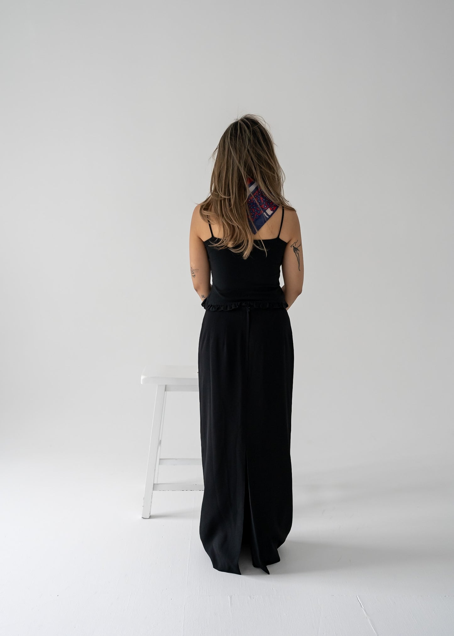 Person wearing a vintage black tank top with a ruffle hem and black column skirt in a studio setting.