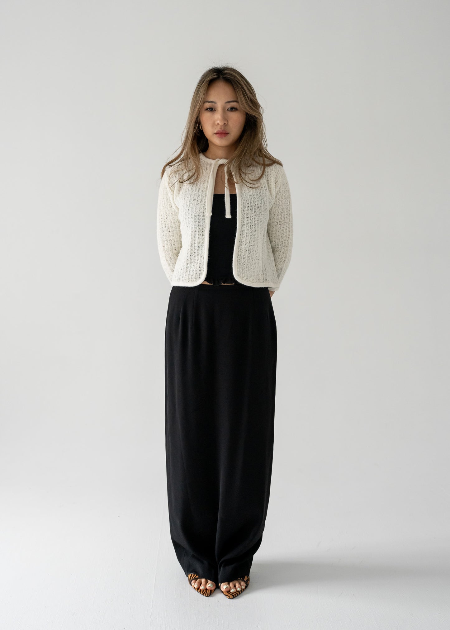 Woman wearing a vintage white knit cardigan and vintage black column skirt  on a plain background