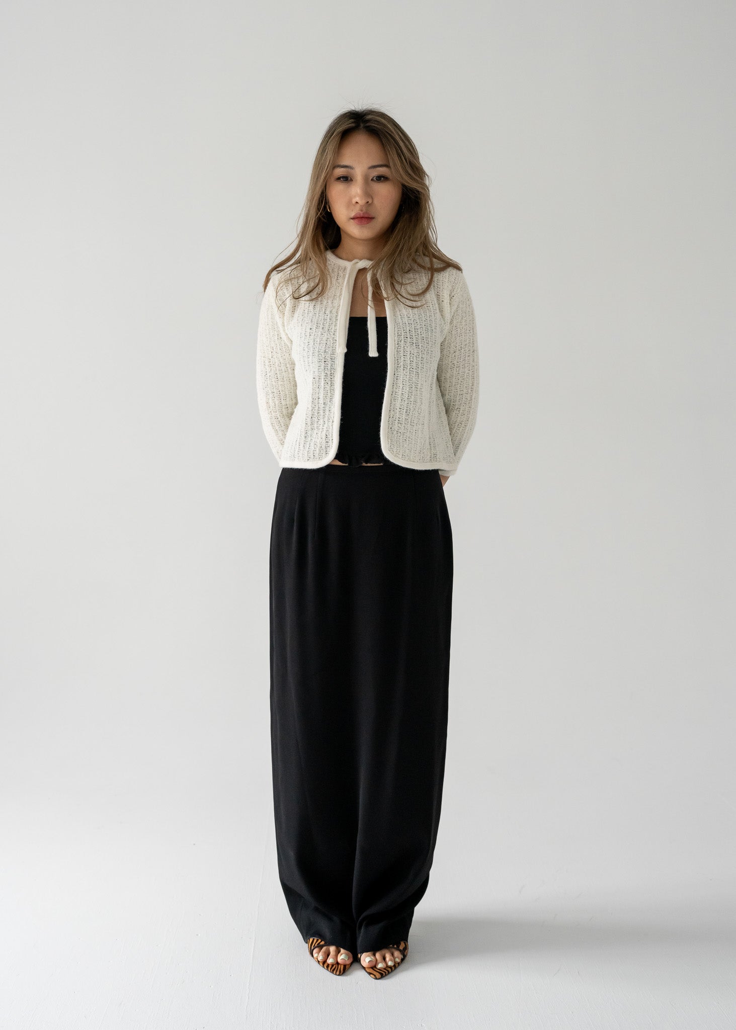 Woman wearing a vintage white knit cardigan and vintage black column skirt  on a plain background
