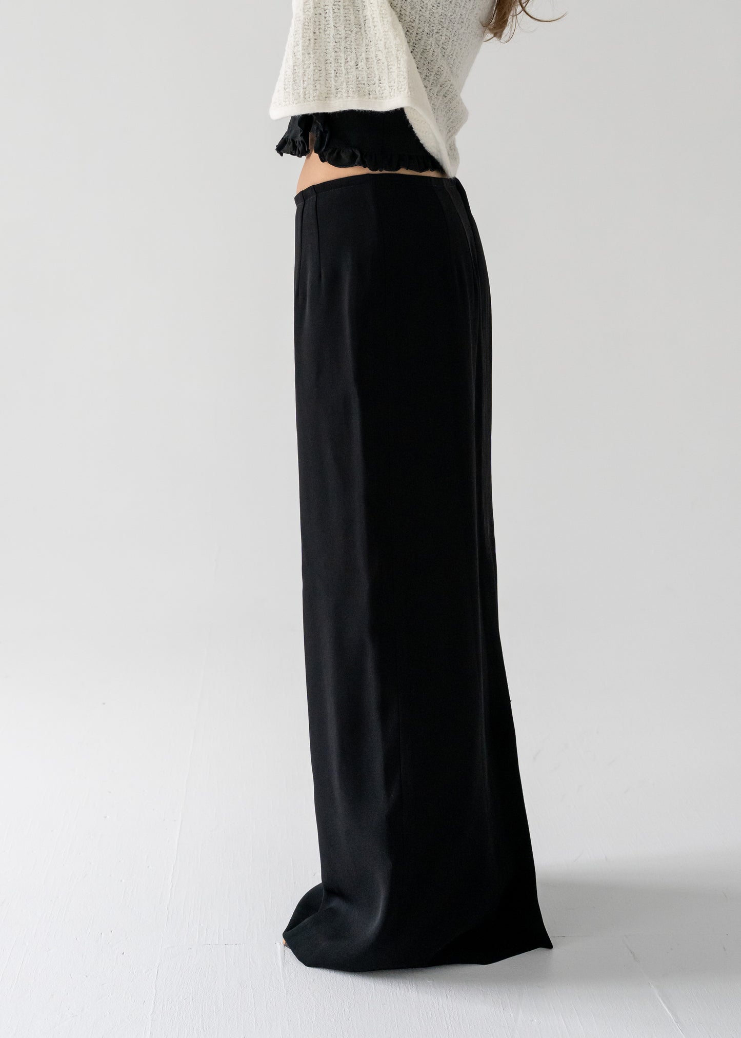 A person standing sideways, wearing a vintage fitted column maxi skirt with a center back slit, paired with a cream top.
