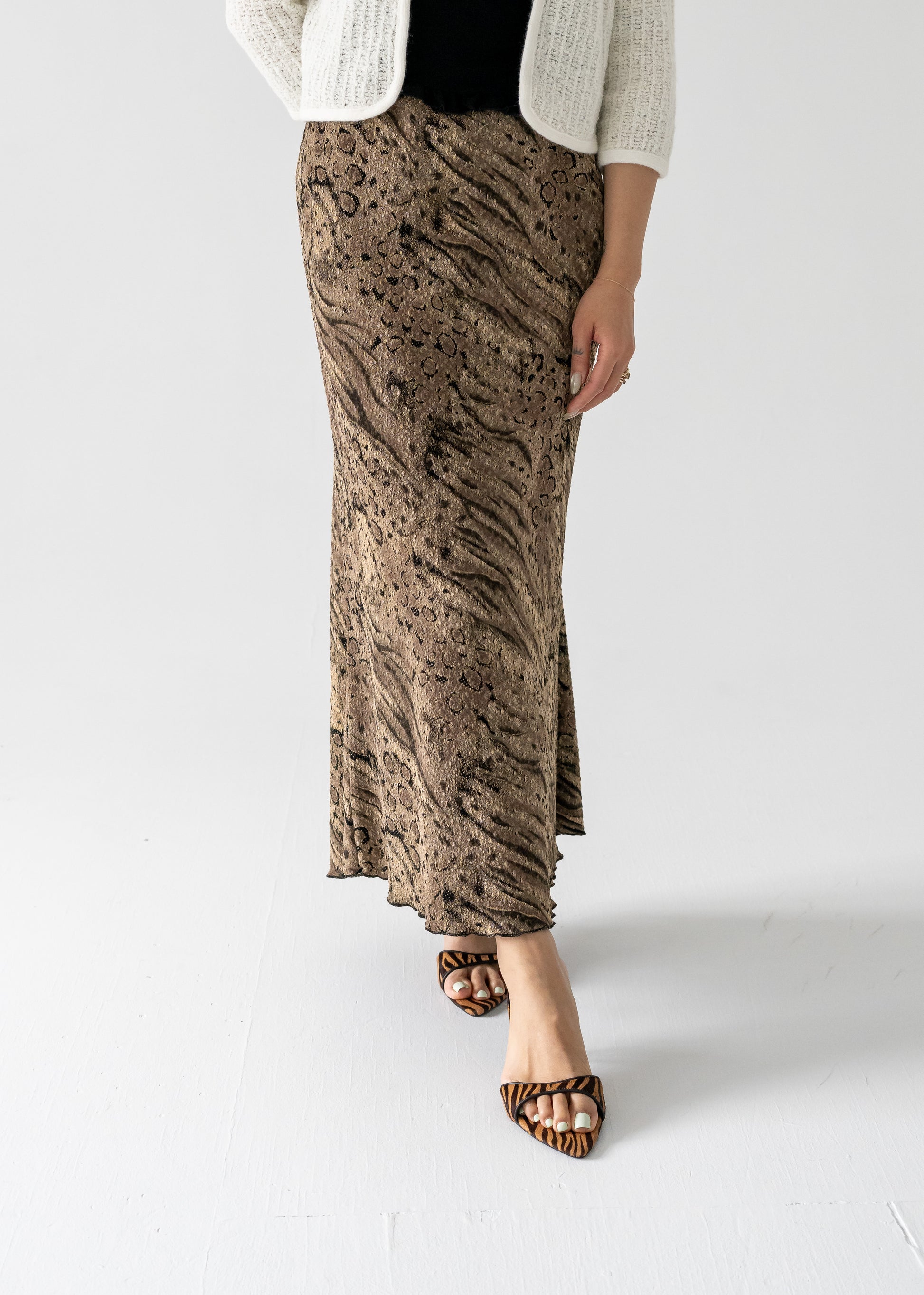 A model wearing a vintage bronze and black abstract animal print stretch scallop bottom maxi skirt with a banded elastic waist and a lettuce hem.