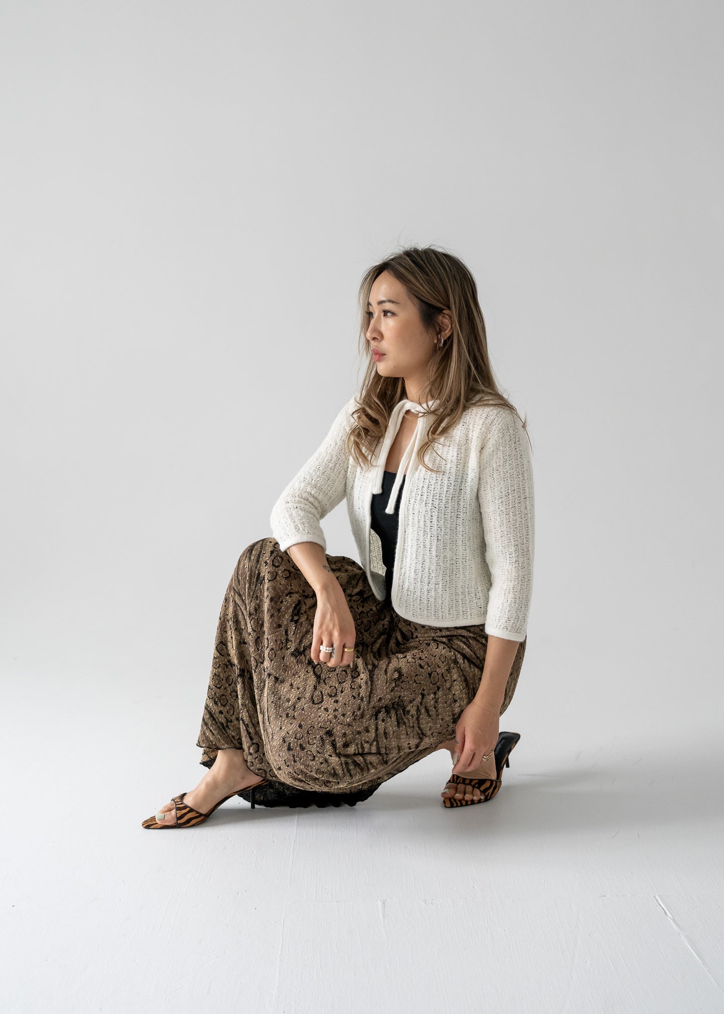 Woman in vintage long maxi skirt with a bronze and black abstract animal print and cream cardigan sitting on the floor against a plain background