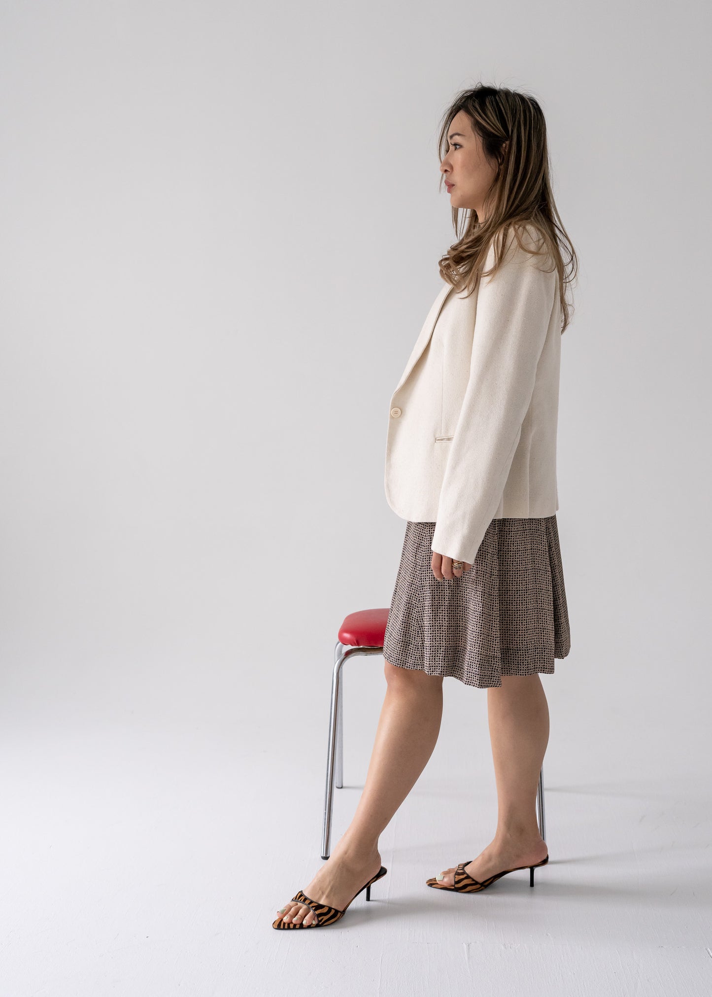 Woman in cream blazer and vintage patterned skirt standing against a plain background