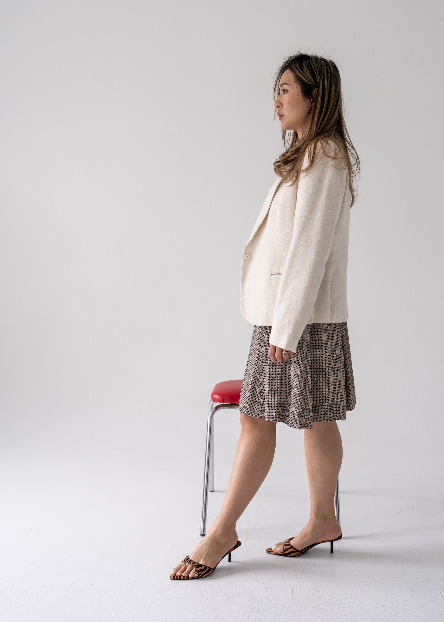 Woman in cream blazer and vintage patterned skirt standing against a plain background