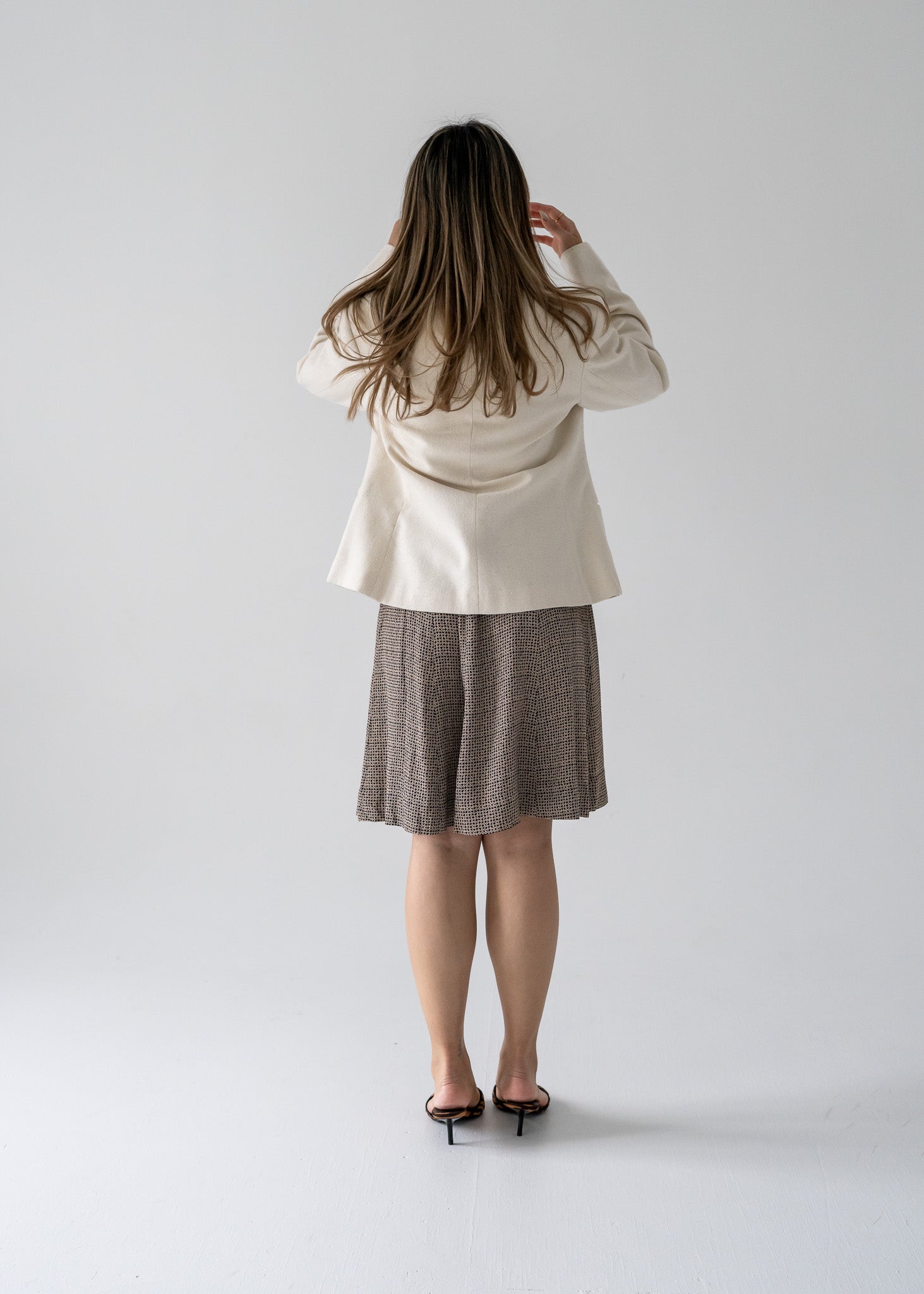 Person wearing a cream blazer and vintage black and beige floral print mini swing skirt on a white background