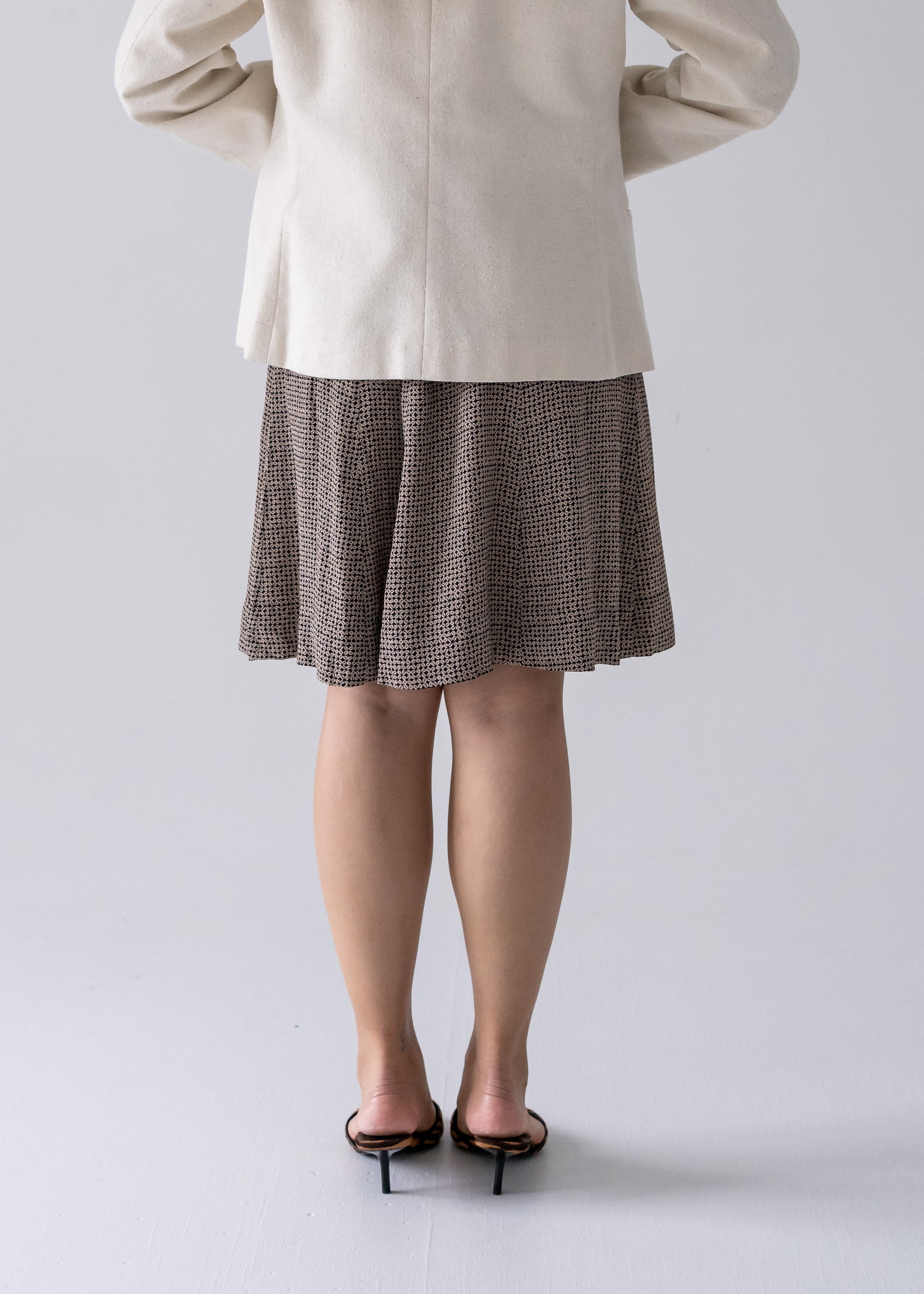 A person wearing a vintage cream-colored, one-button blazer with pockets, paired with a patterned skirt 