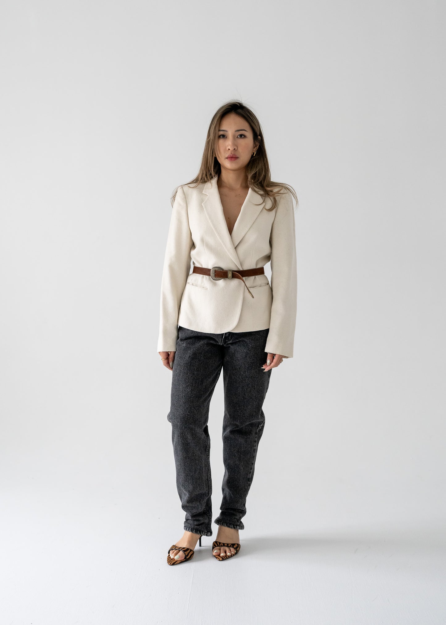 A model wearing a vintage cream-colored, one-button blazer with pockets, paired with dark jeans and heels.