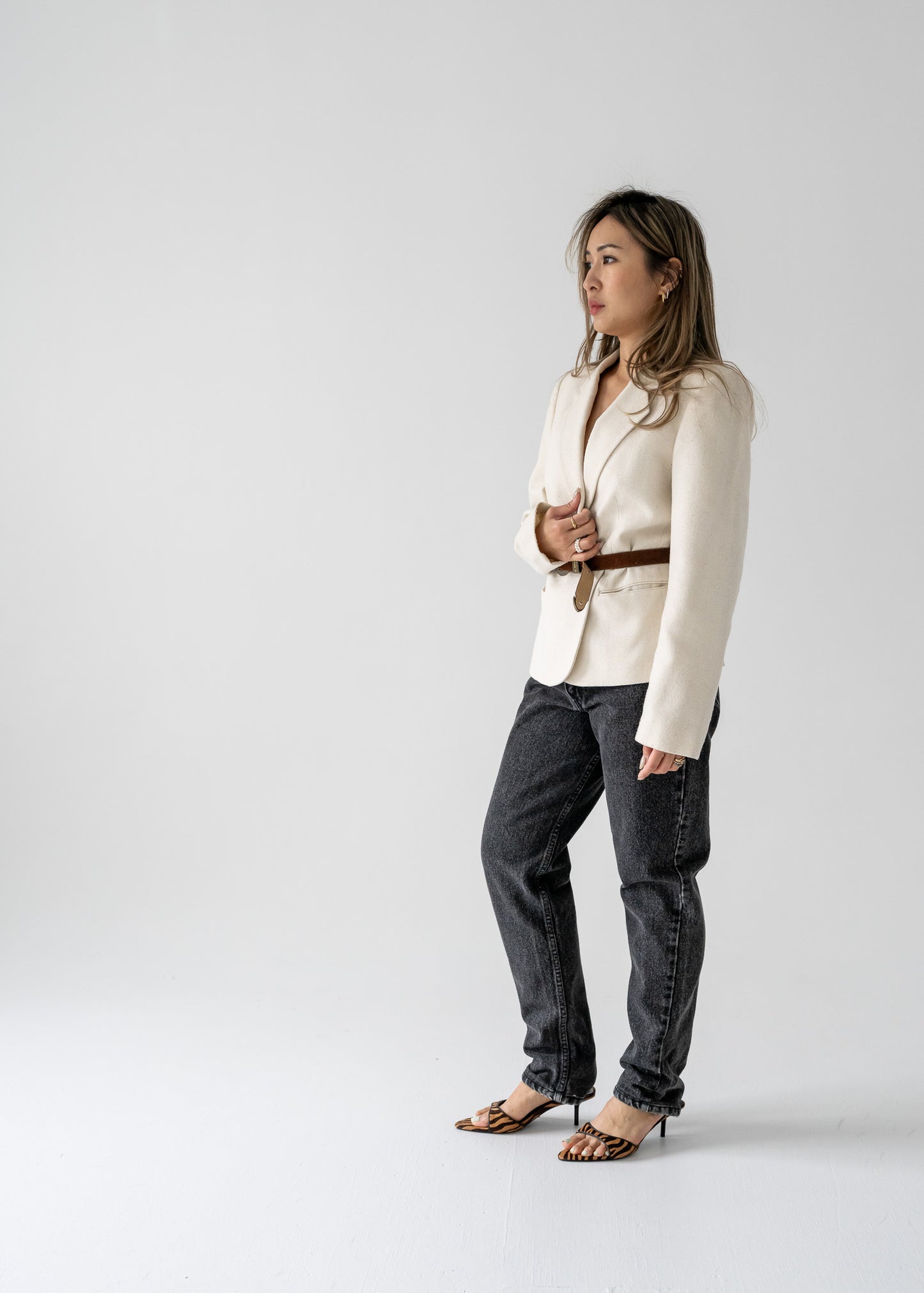 A model wearing a vintage cream-colored, one-button blazer with pockets, paired with dark jeans and heels.