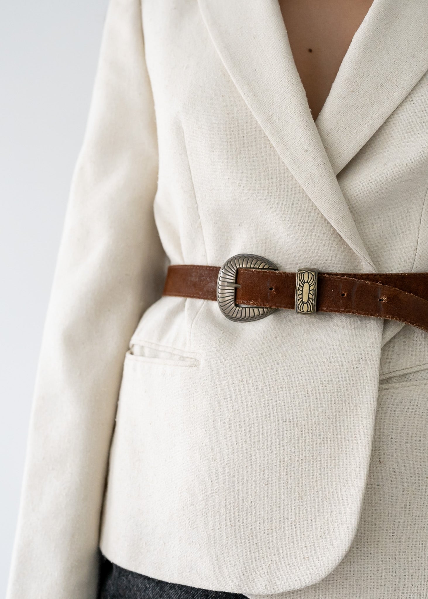 Close-up of a person wearing a vintage cream-colored coat with a brown belt and decorative buckle.