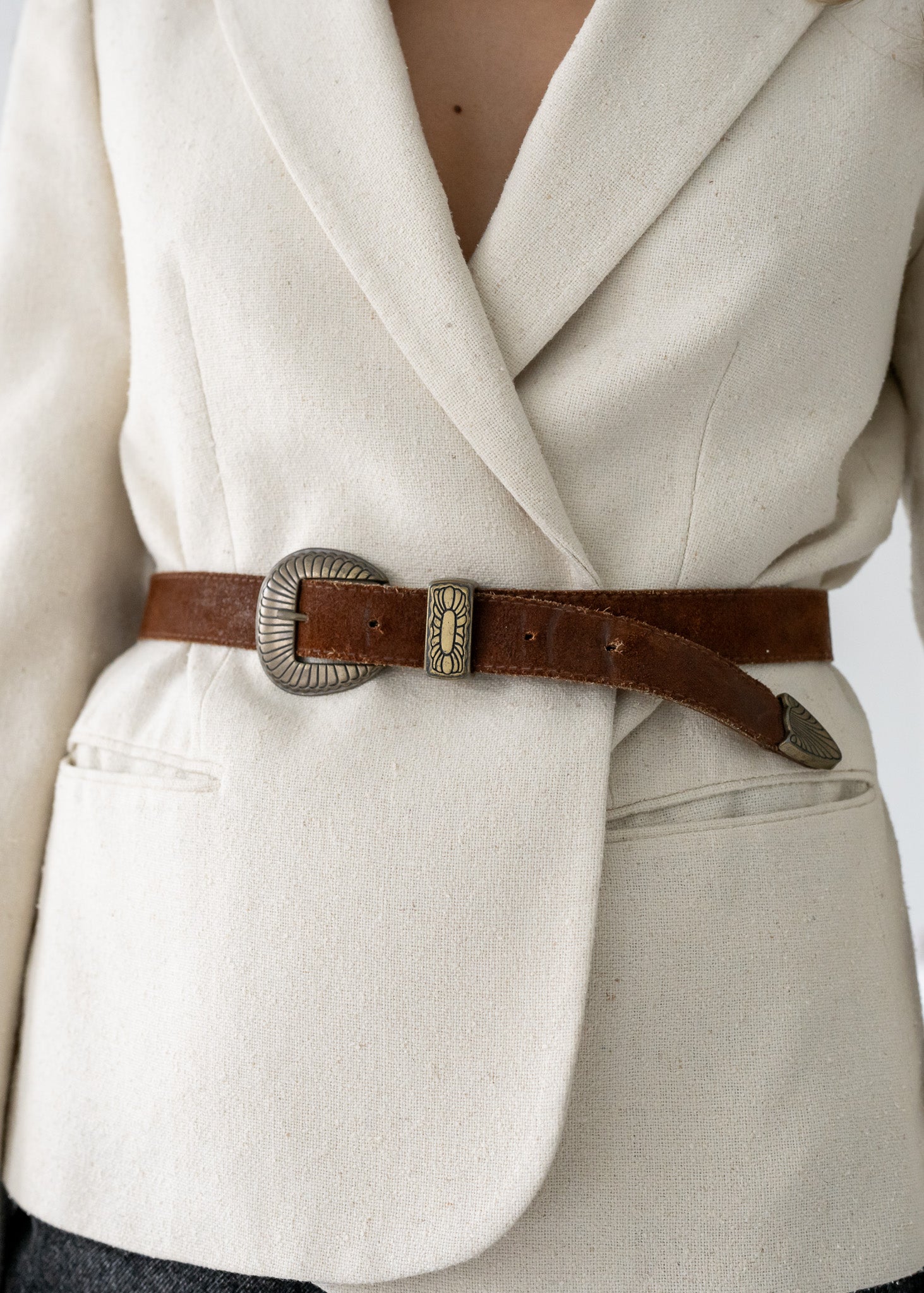 Close-up of a person wearing a beige coat with a brown belt and decorative buckle.