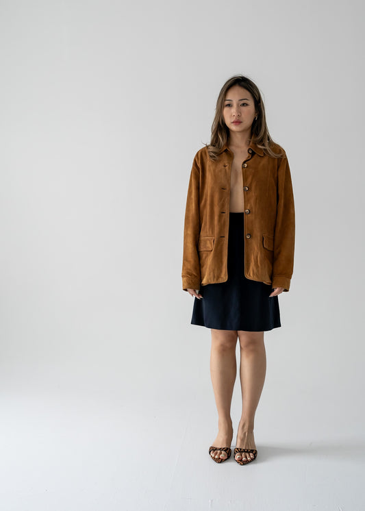 A person wearing a vintage tawny brown suede leather button-up collared jacket with a black mini skirt.