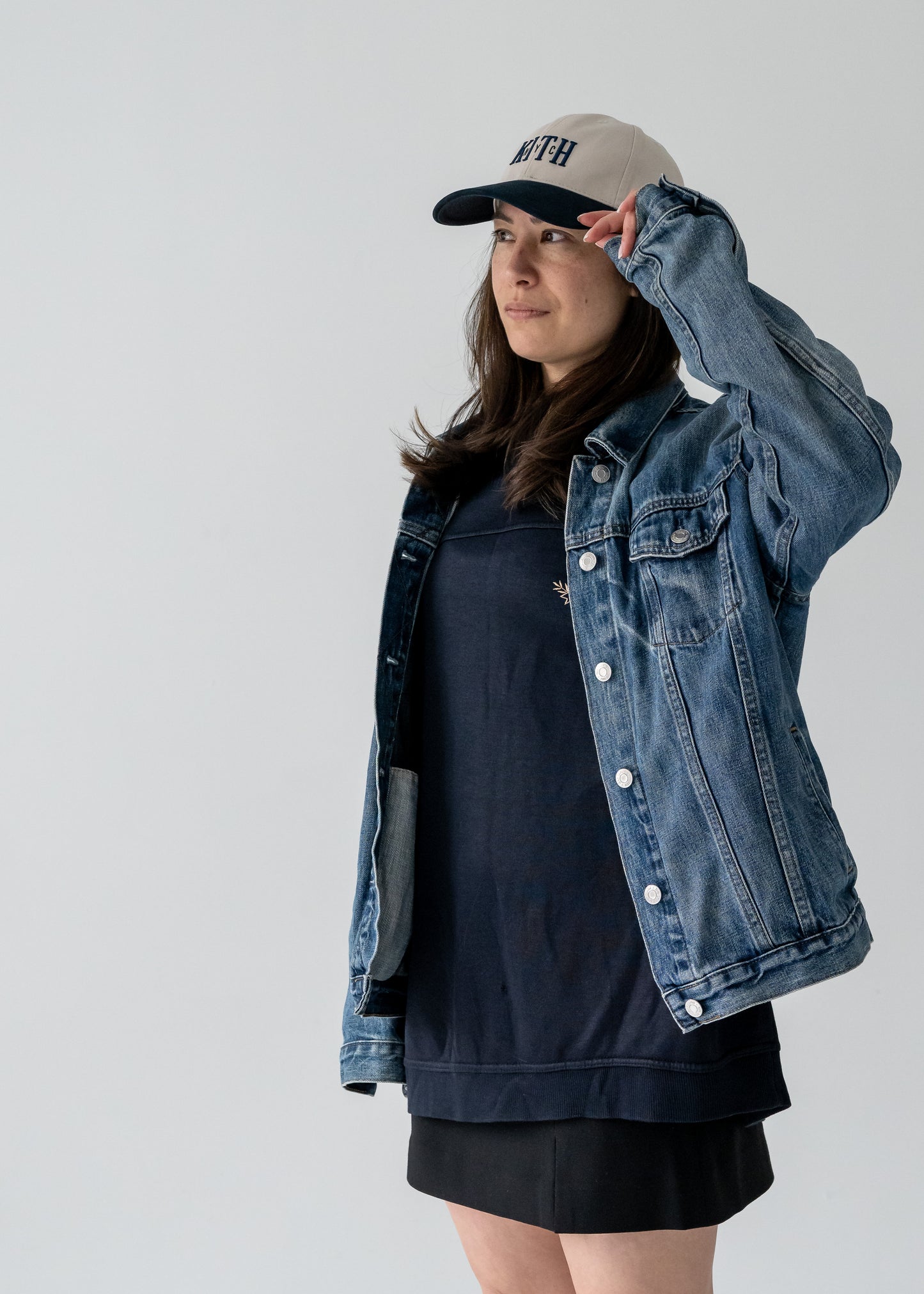 A person wearing a vintage navy and taupe Oscar de la Renta long sleeve pullover shirt with a crew neck, over a black dress, paired with a denim jacket and a beige hat.
