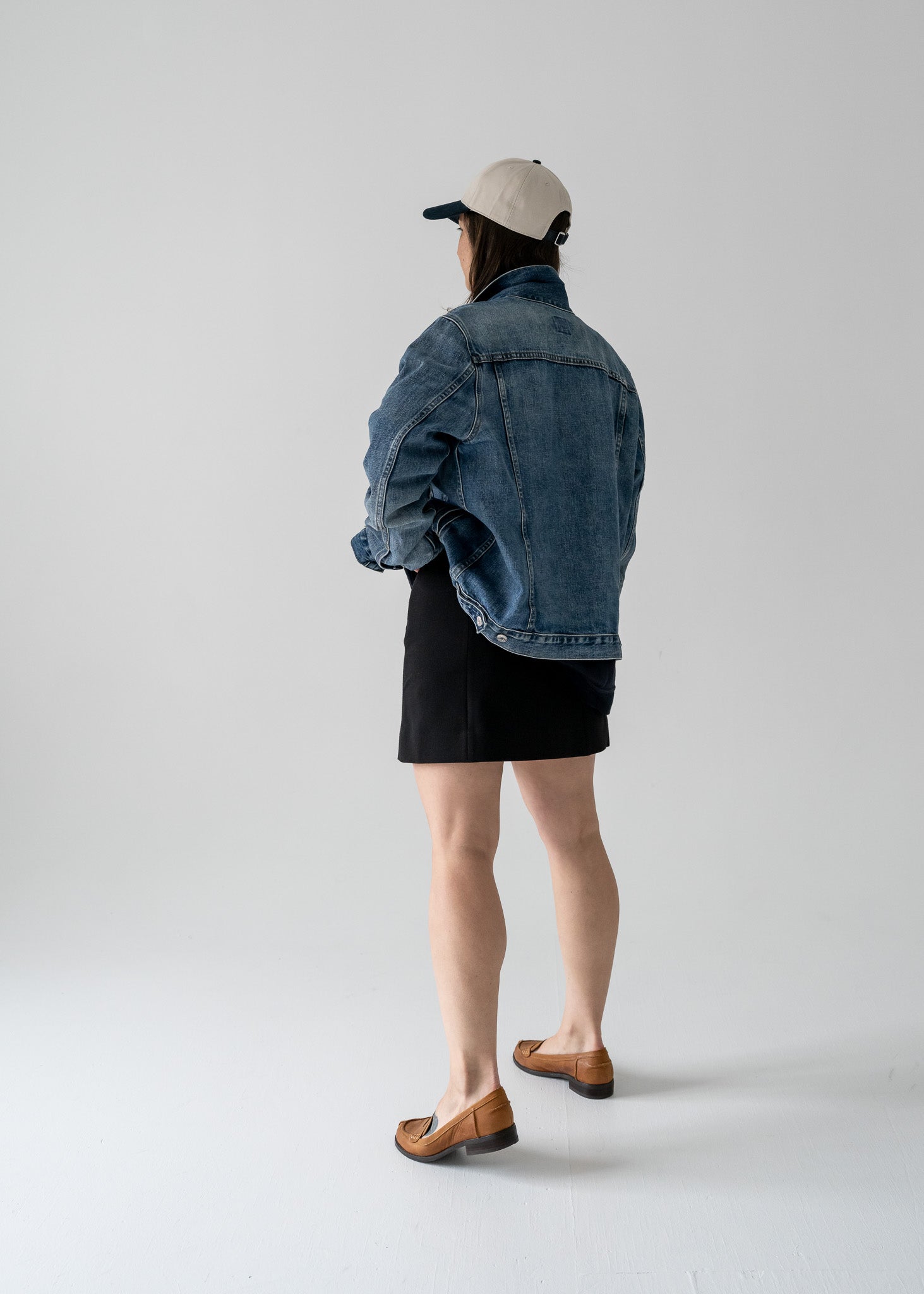 Person wearing a vintage denim jacket and black a skirt with a cap, viewed from the back.