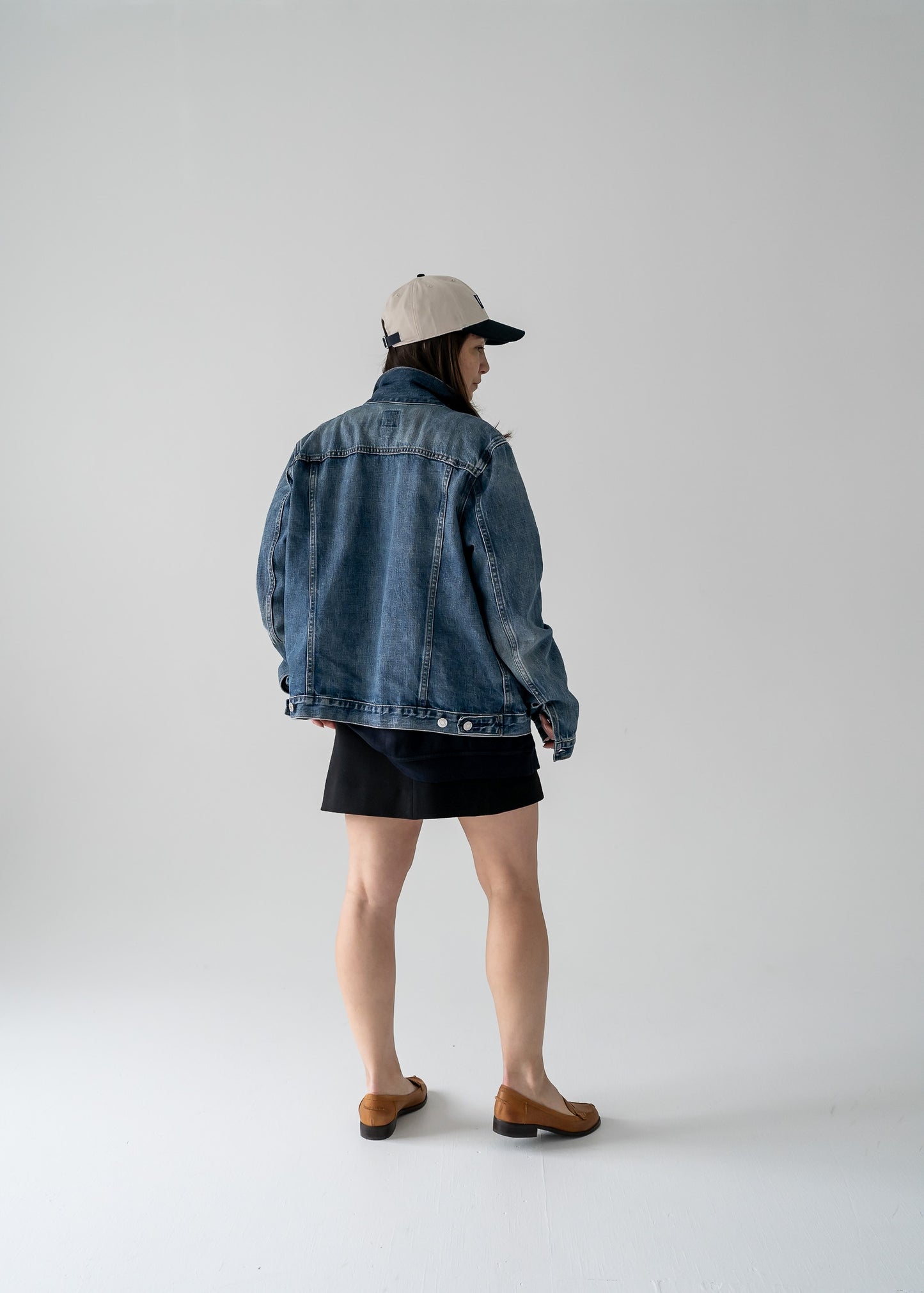 Person wearing a vintage denim jacket and cap on a plain background
