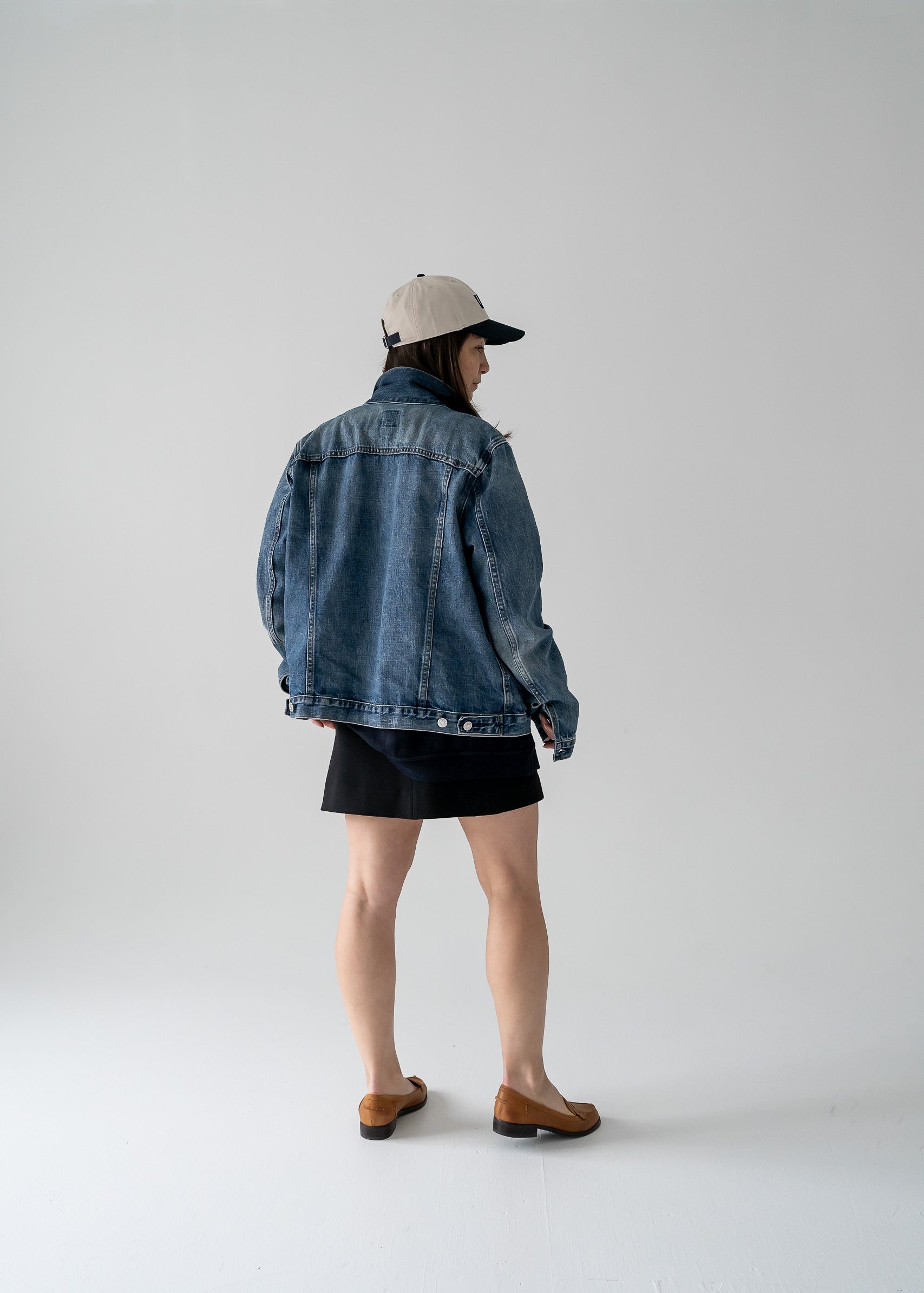 Person wearing a vintage denim jacket and cap on a plain background