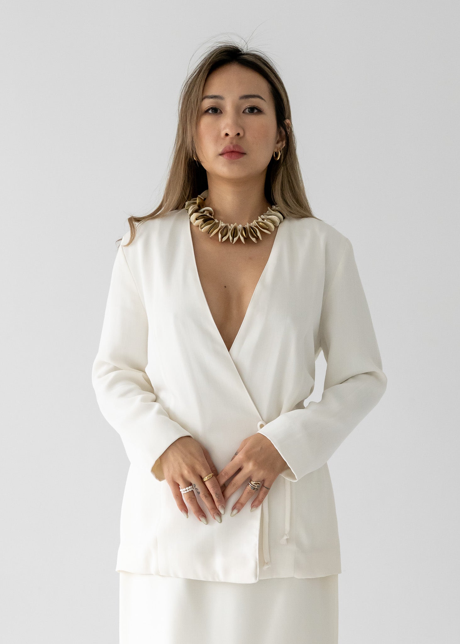 A woman wearing a white slinky rayon 3/4 sleeve tie-back blouse with a deep v-neck and long sleeves, paired with a matching skirt.