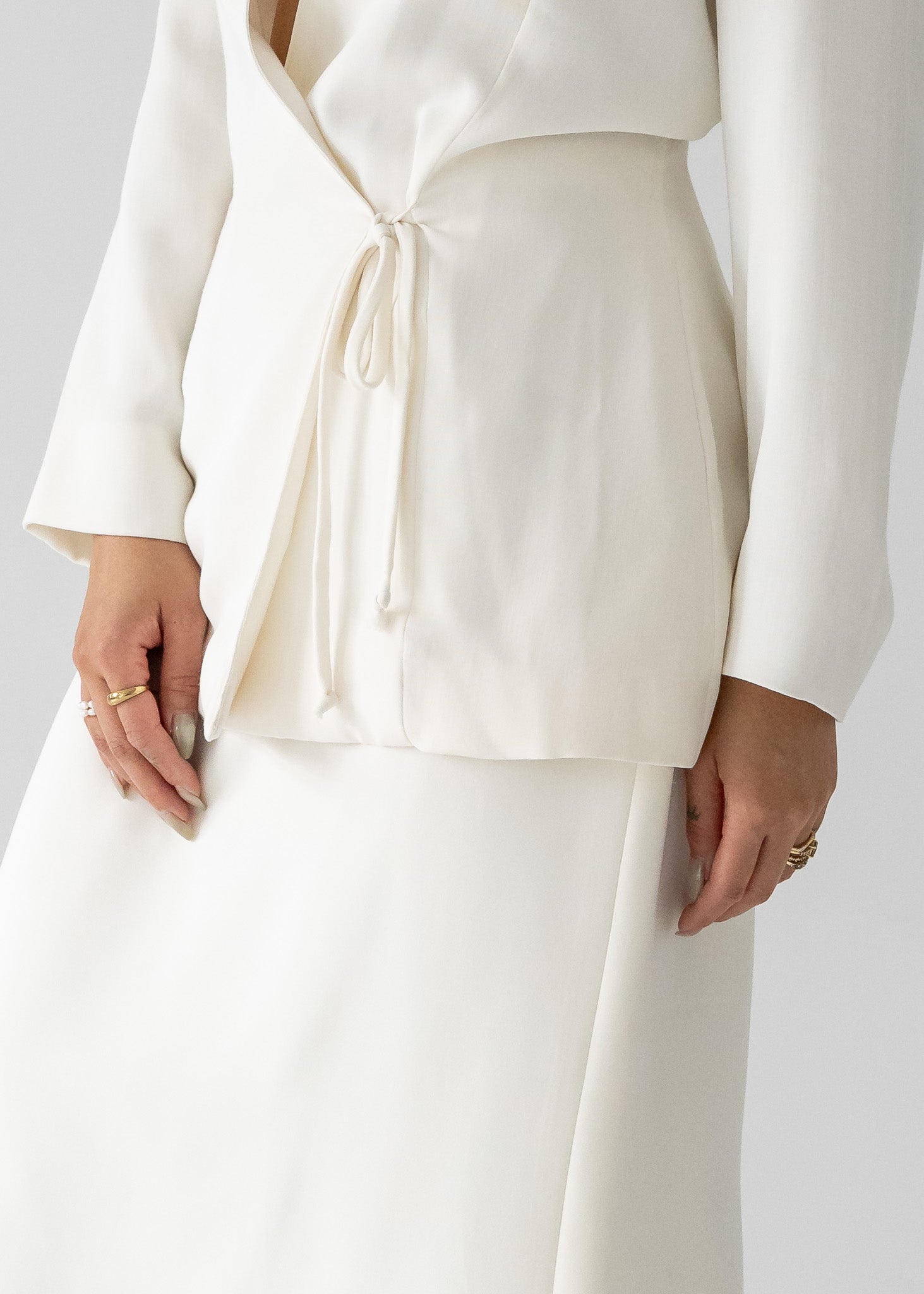 A woman modeling a white slinky rayon long sleeve tie-back blouse with a cinched waist at the center back and a white column skirt. 