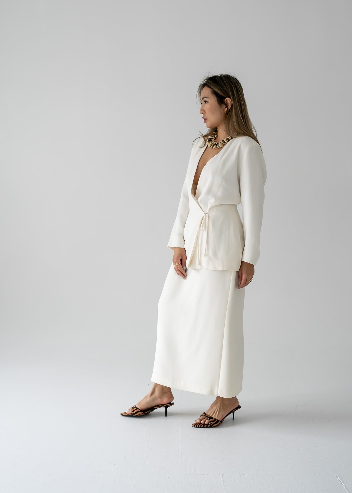 Woman in a white wrap blouse and vintage cream long line skirt with a centre back slit and a dainty beaded band standing against a plain background