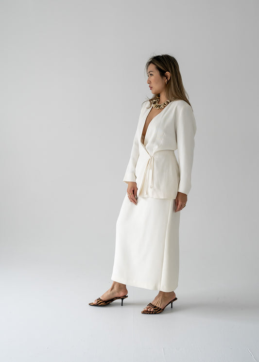 Woman in a white wrap blouse and vintage cream long line skirt with a centre back slit and a dainty beaded band standing against a plain background