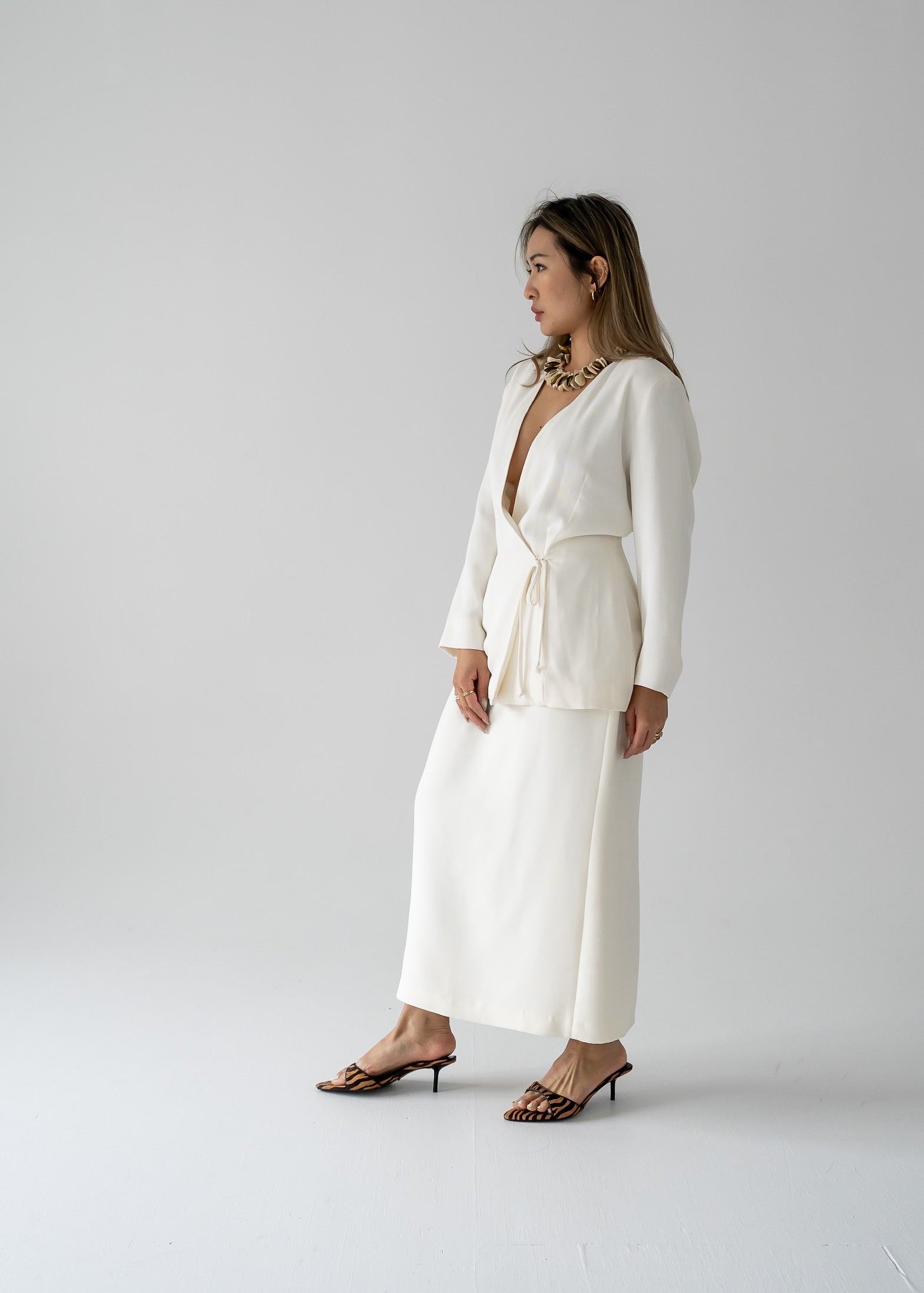 A woman modeling a white slinky rayon 3/4 sleeve tie-back blouse with a deep V-neck and a cinched waist at the center back.