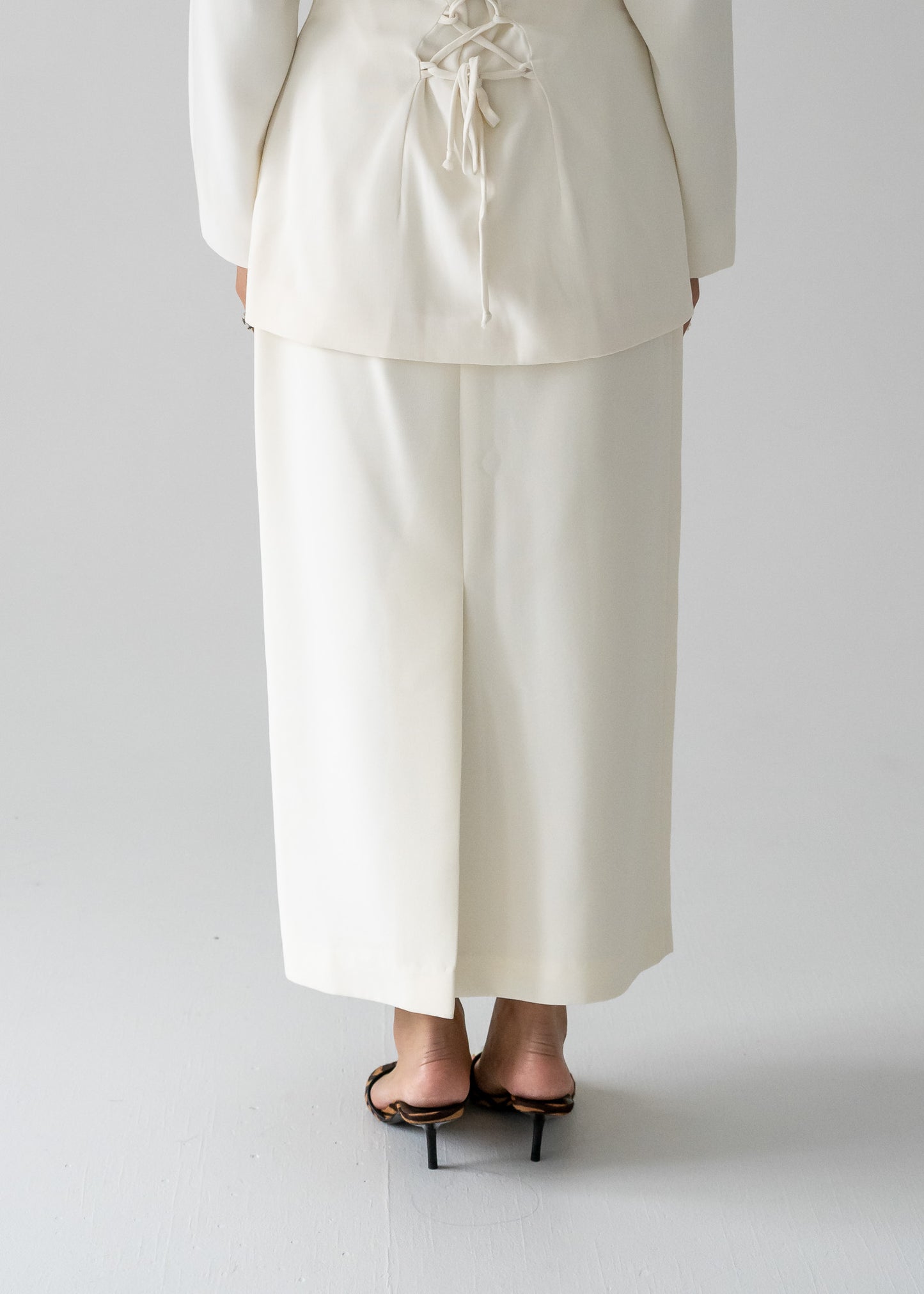 Person wearing a white lace up blouse and vintage cream long line skirt with a centre back slit and a dainty beaded band on a plain background