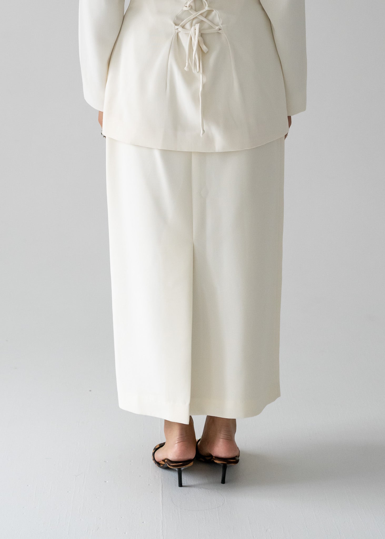 Person wearing a white lace up blouse and vintage cream long line skirt with a centre back slit and a dainty beaded band on a plain background