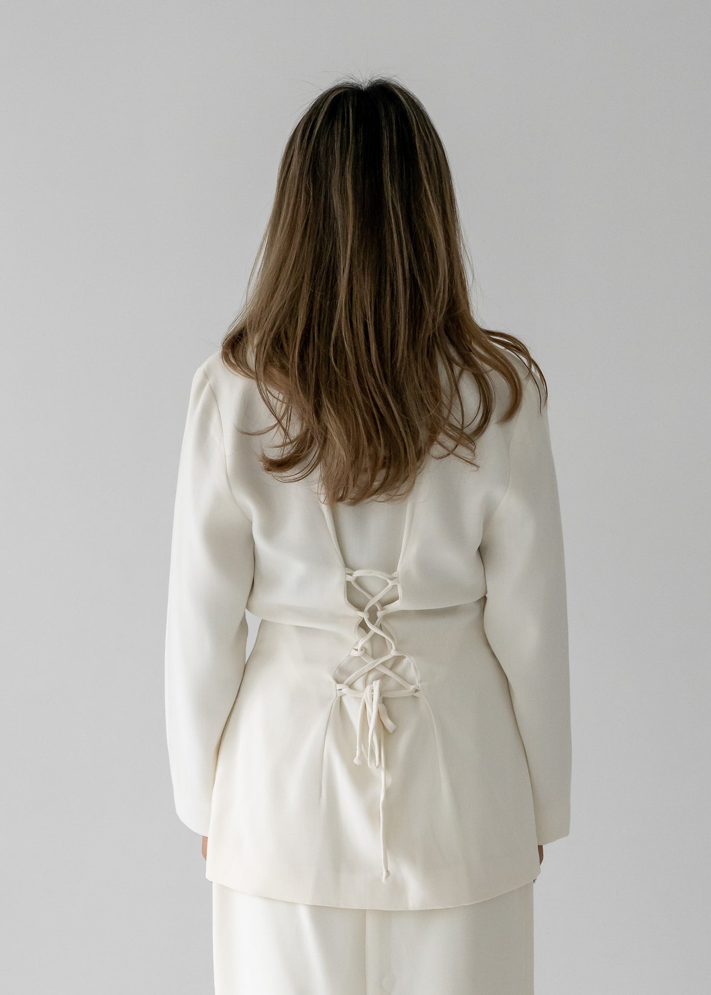 Person wearing a white blouse with a white lace-up back against a plain background