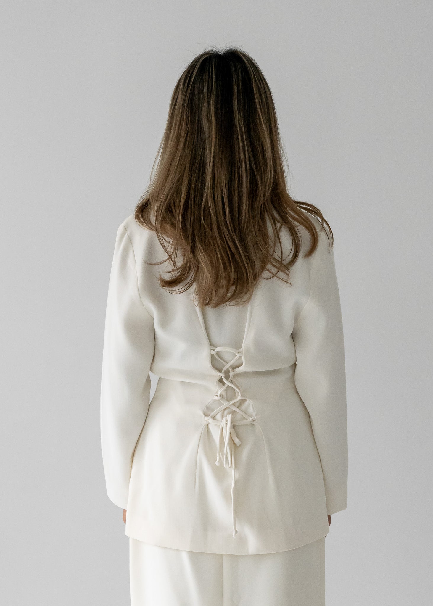 Person wearing a white blouse with a white lace-up back against a plain background