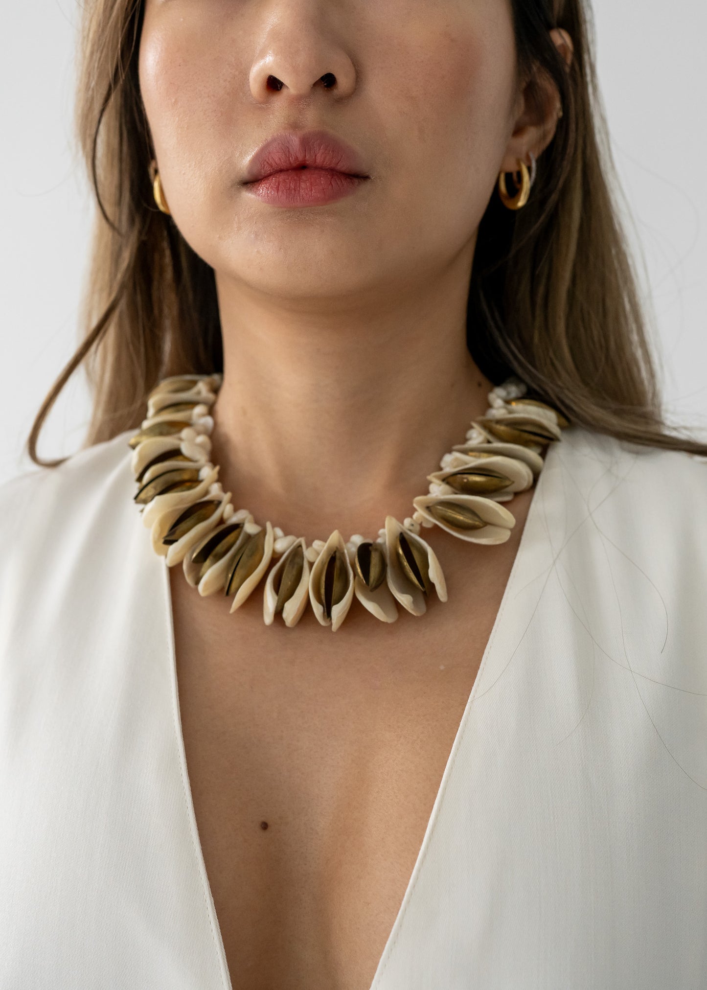A person wearing a shell and brass chunky necklace with pale cream natural shells and brass-toned metal, displayed in an allover shot.