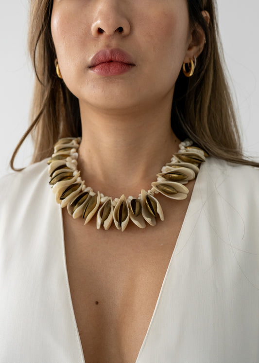 A person wearing a shell and brass chunky necklace with pale cream natural shells and brass-toned metal, displayed in an allover shot.