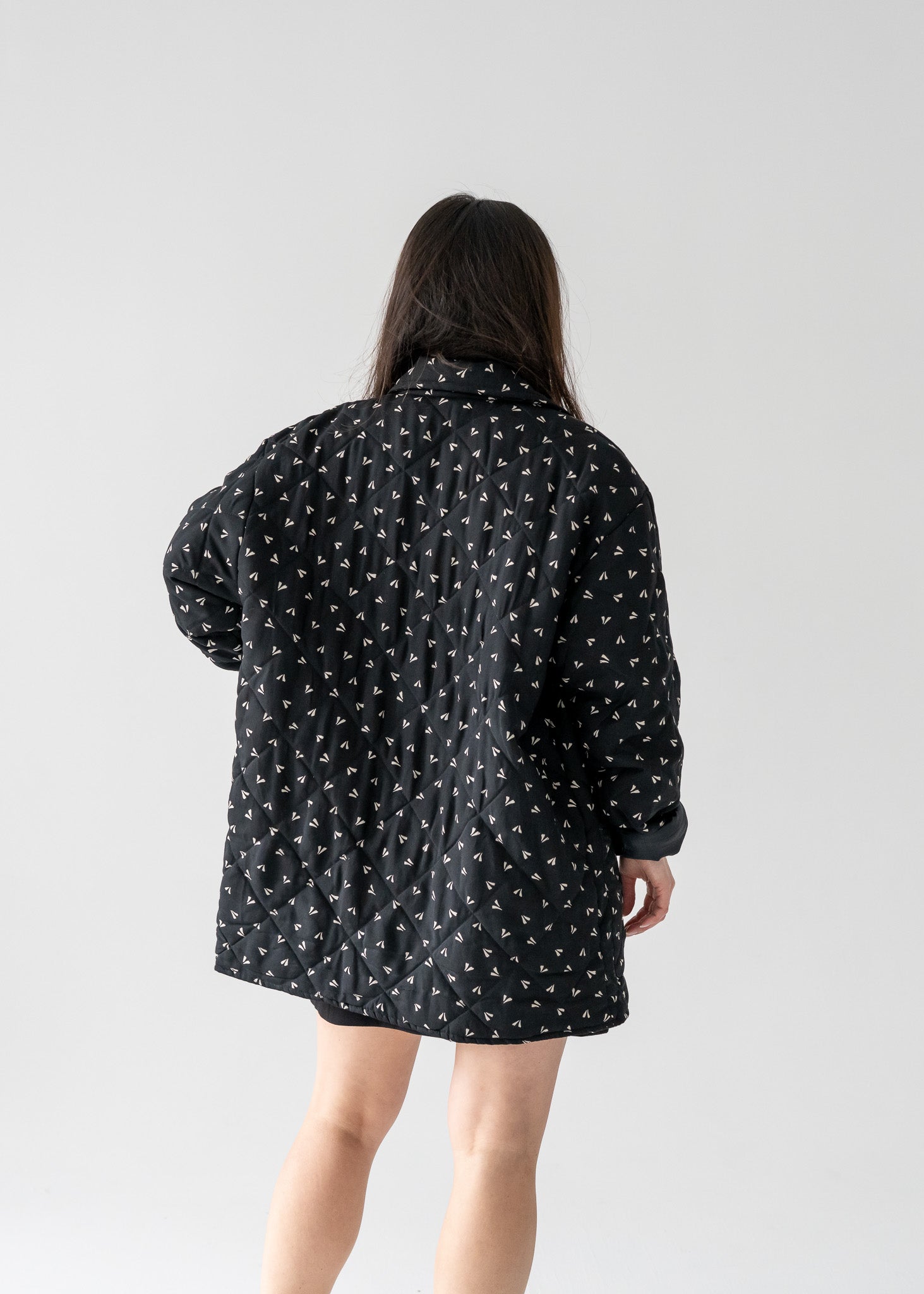 Person wearing a vintage black and beige small leaf print silk quilted lightweight jacket with long sleeves and a classic collar against a white background