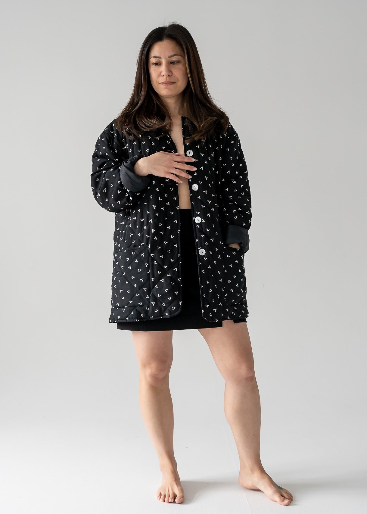 Woman wearing a vintage black and beige small leaf print silk quilted lightweight jacket with long sleeves and a classic collar on a plain background