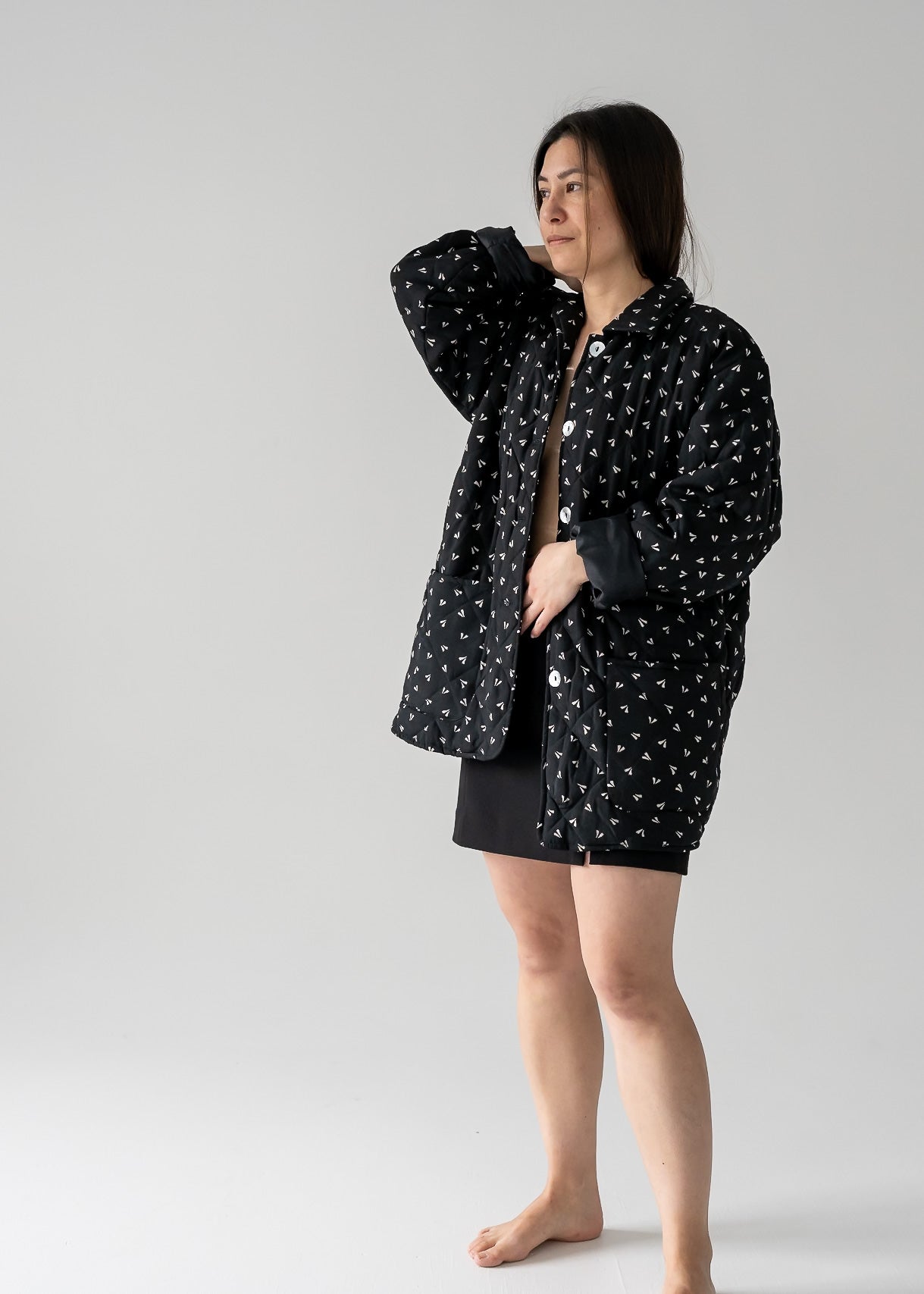 A woman standing, wearing a vintage black and beige small leaf print silk quilted lightweight jacket with long sleeves and a classic collar.