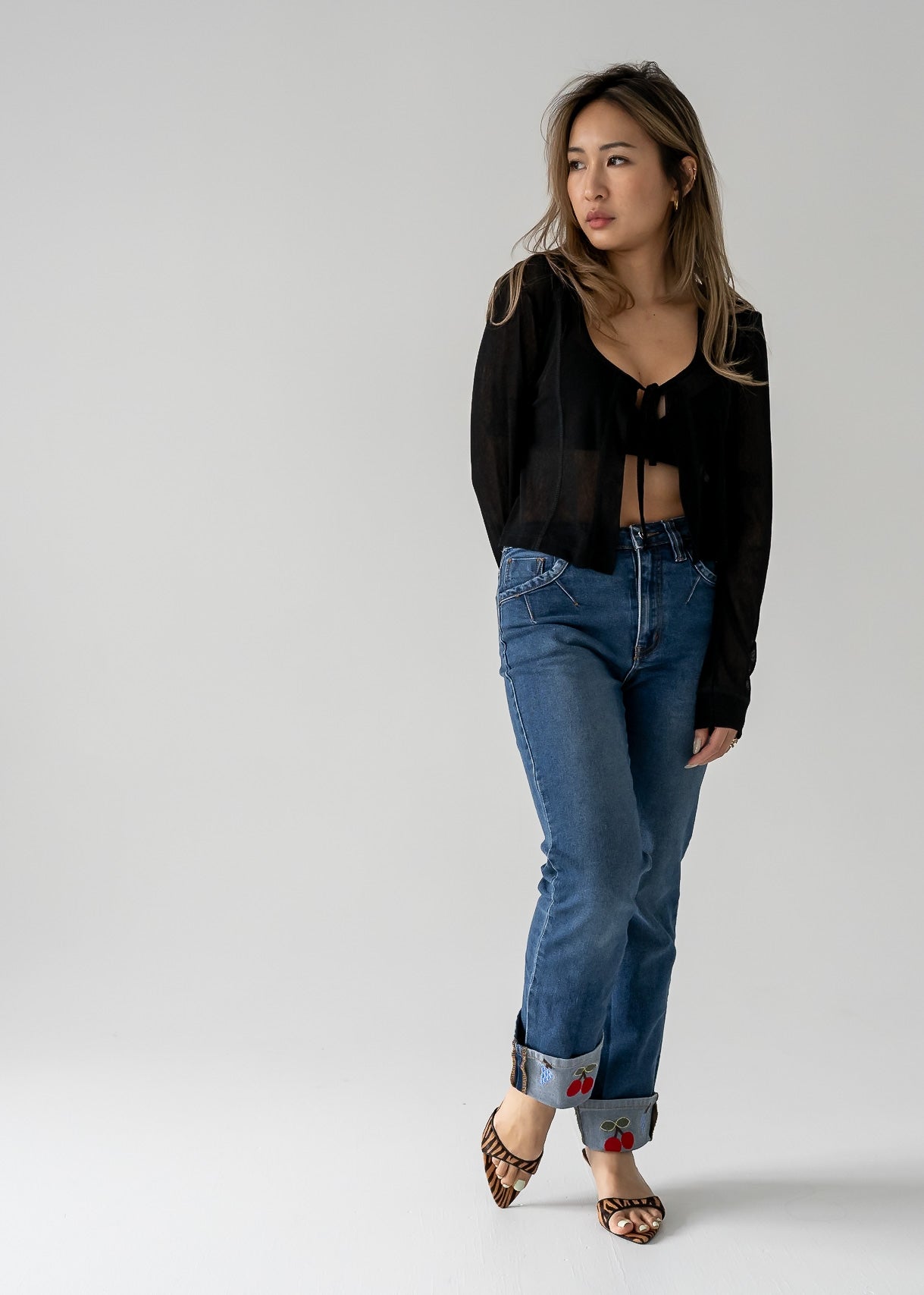 A person standing against a white background, wearing vintage medium wash blue jeans with cuffed hem and a black top.