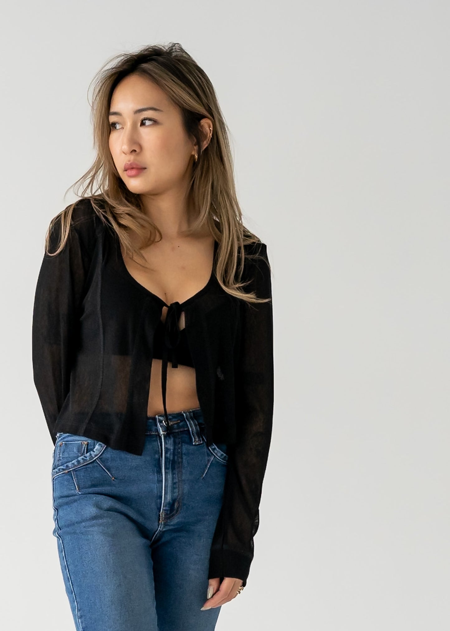 Person wearing vintage medium wash blue jeans with cuffed hem and a black sheer cardigan against a white background