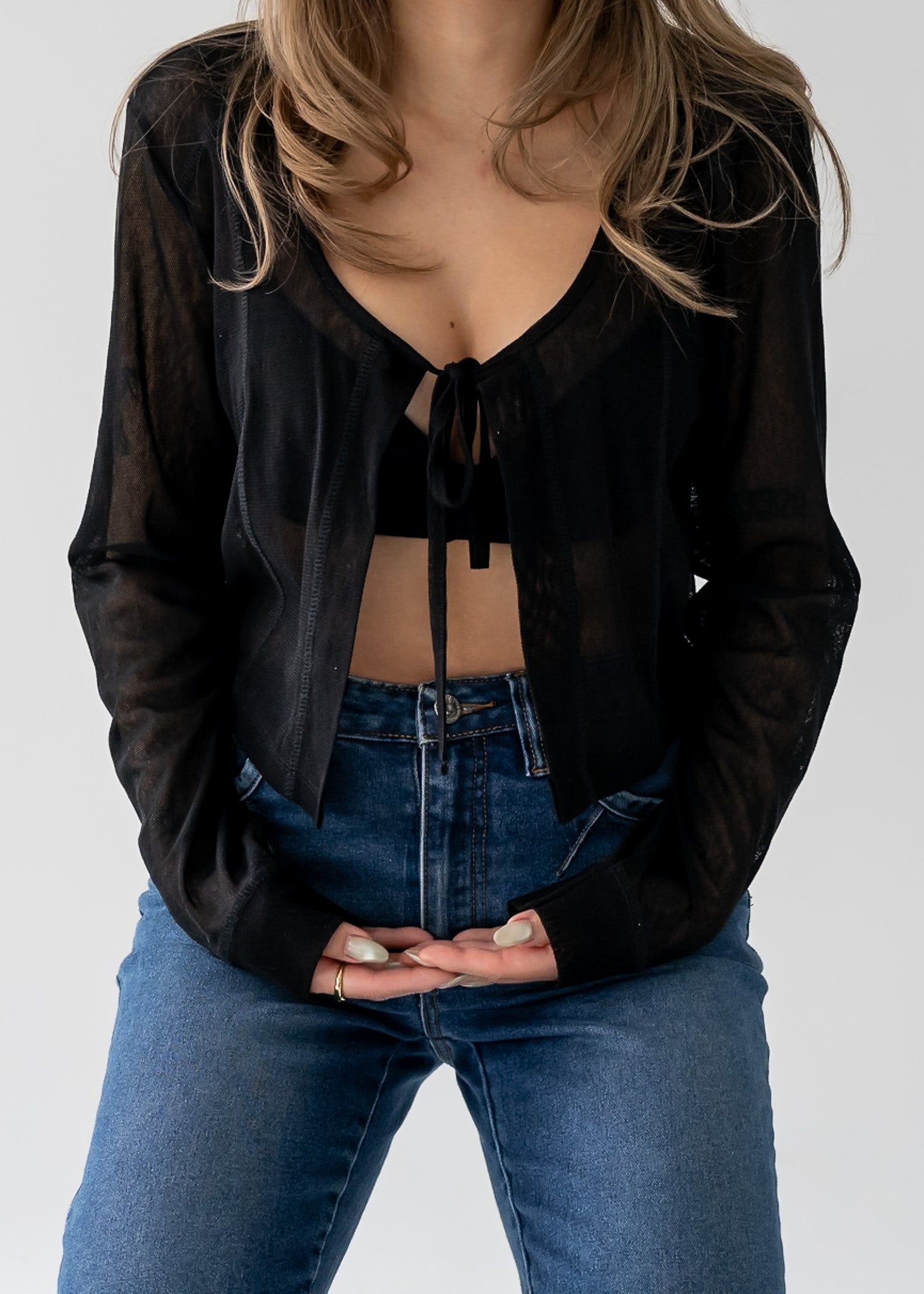 Person wearing vintage medium wash blue jeans with cuffed hem and a sheer black cardigan against a white background