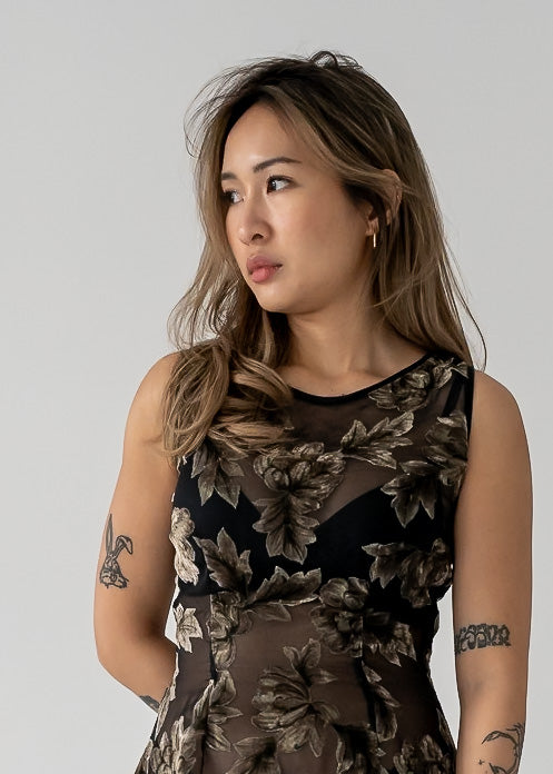 Woman wearing a vintage dark green and black floral velvet burnout sheer sleeveless mini dress against a plain background