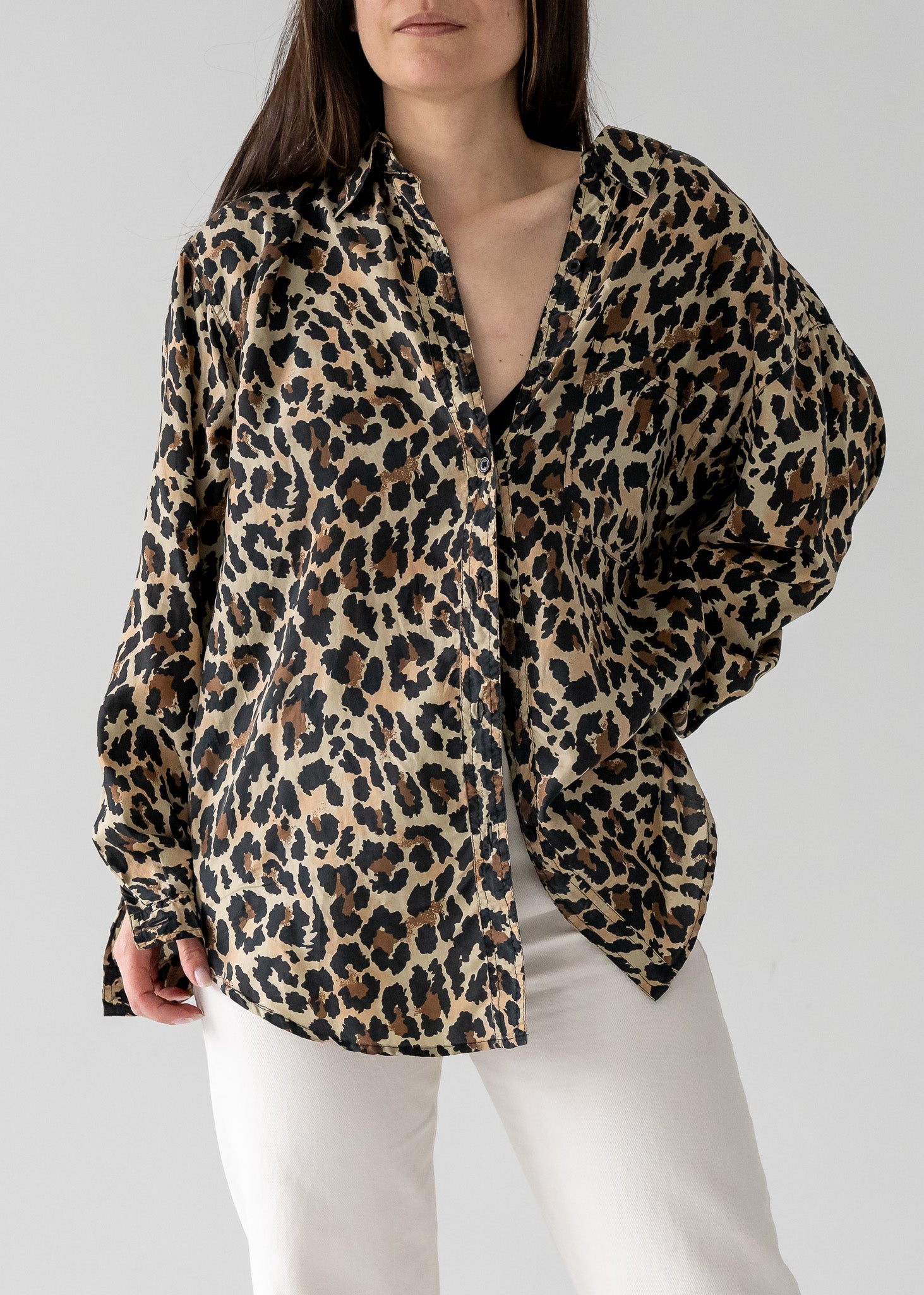Person wearing a vintage silk leopard animal print long sleeve button up blouse with white pants on a plain background