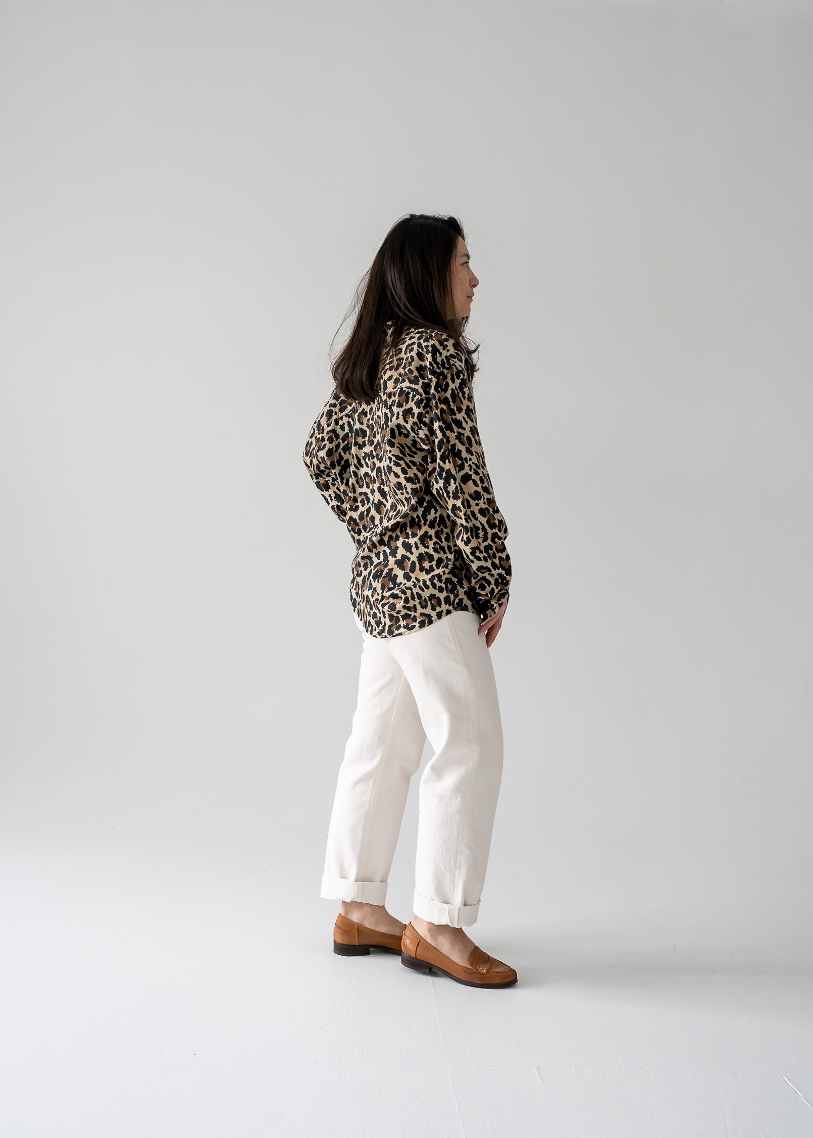 Person wearing a vintage silk leopard animal print long sleeve button up blouse and white pants against a plain background