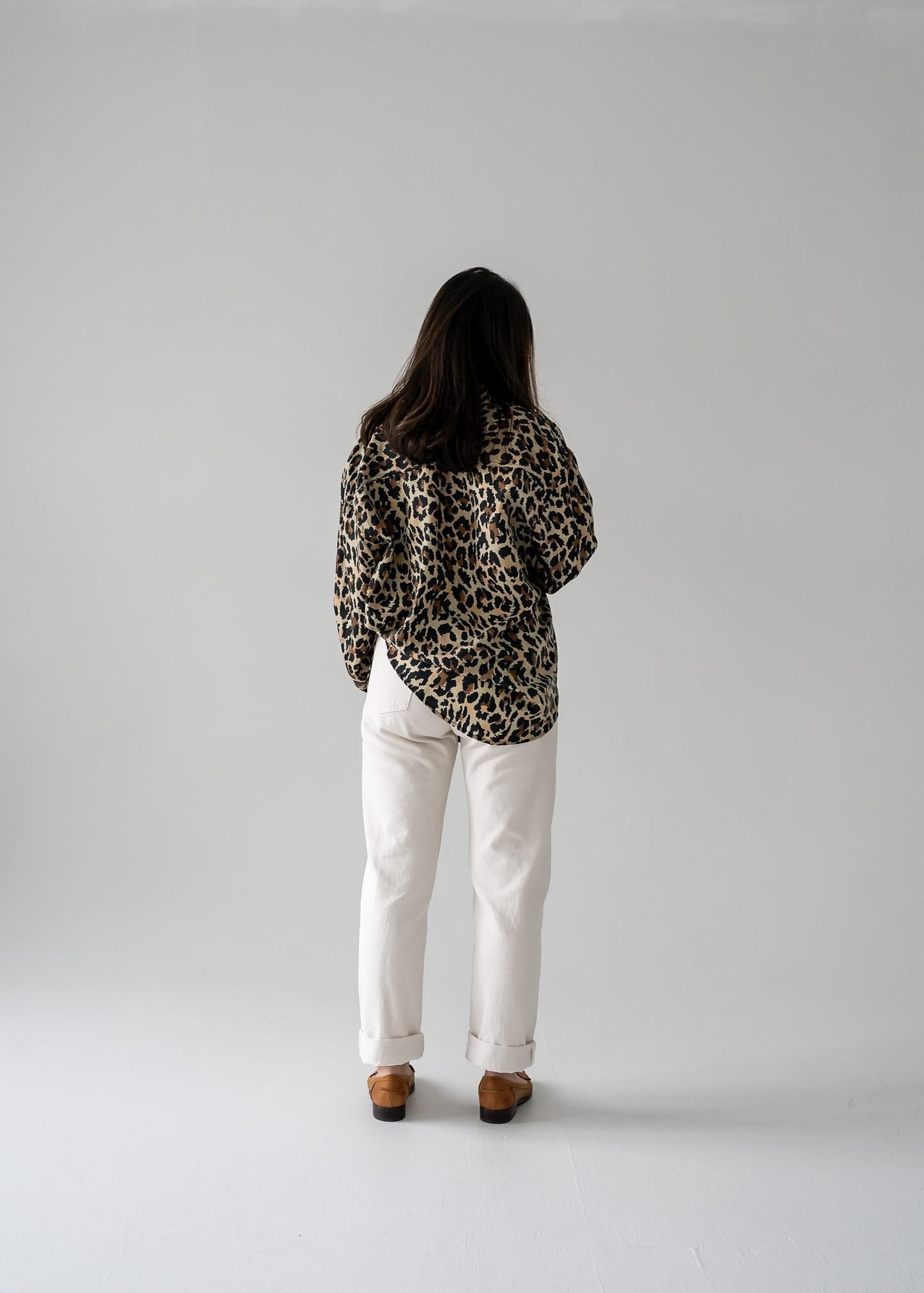 Person wearing a vintage silk leopard animal print long sleeve button up blouse and white pants in a studio setting.