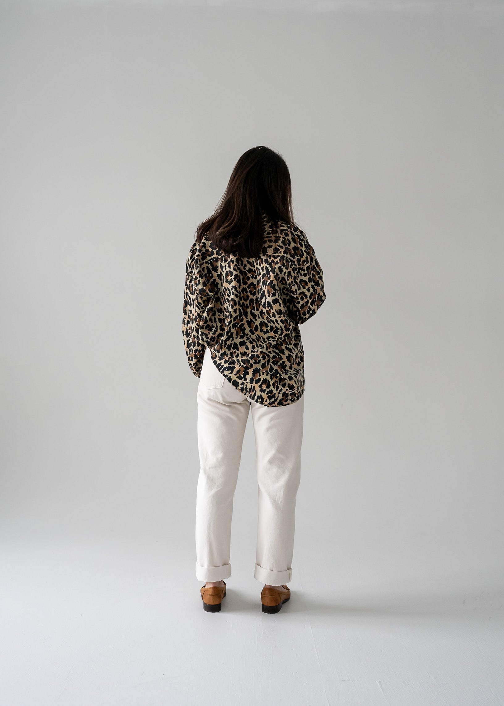 Person wearing a vintage silk leopard animal print long sleeve button up blouse and white pants in a studio setting.