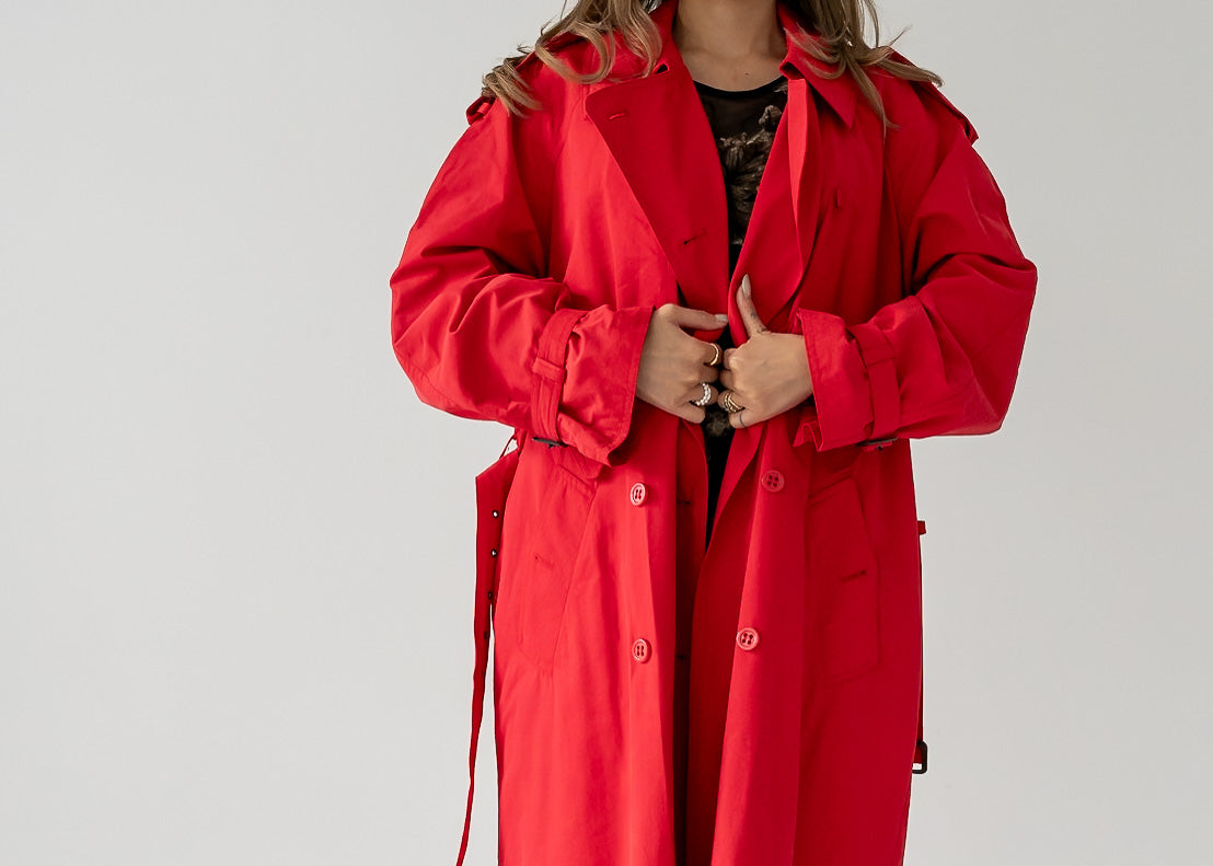 A person wearing a vintage cherry red double breasted button up belted full length trench coat.