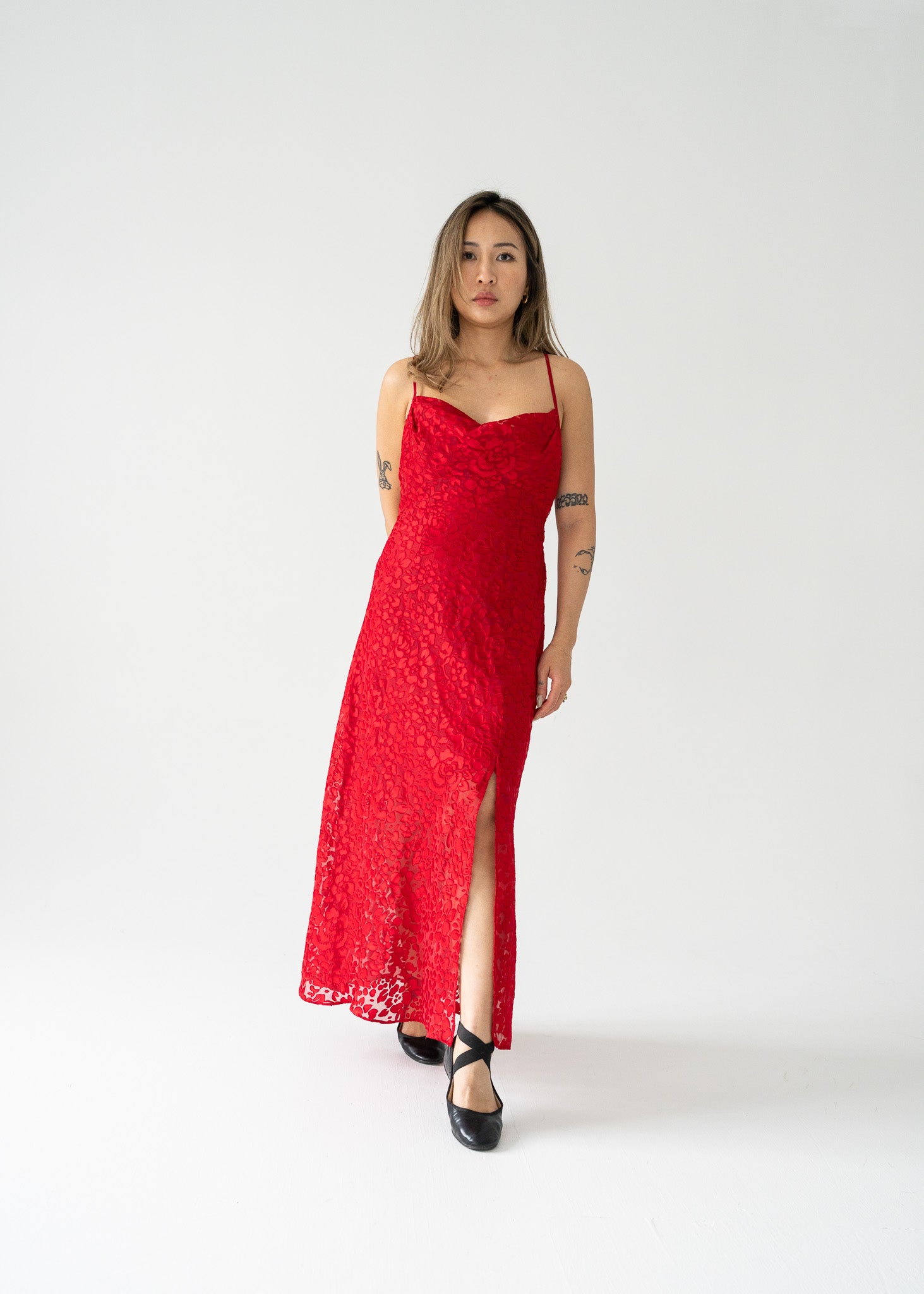 A model wearing a cherry red sheer floral burnout cowl neck thin strap dress with a vertical slit on the left side.